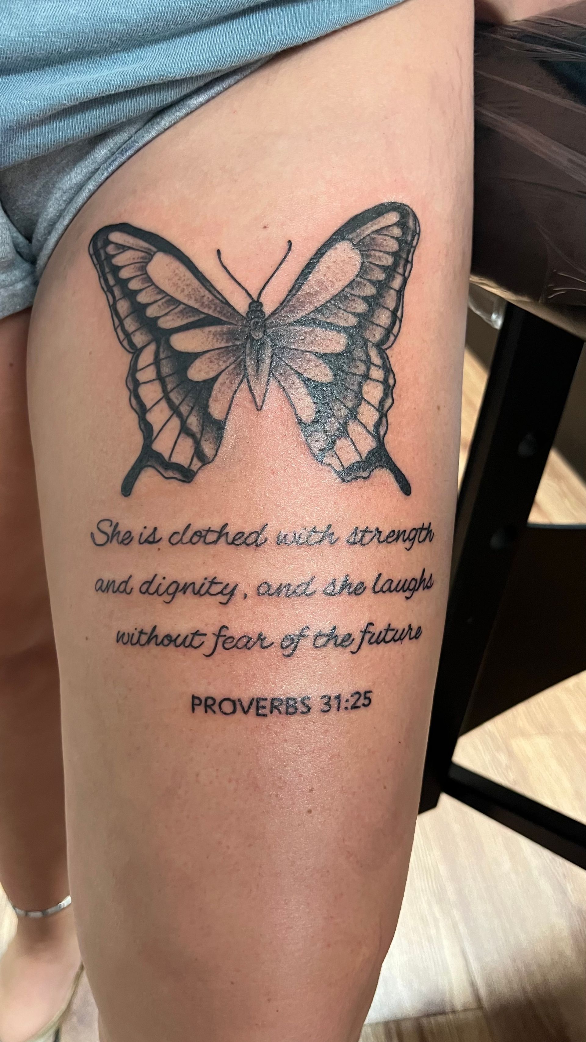 A woman has a tattoo of a butterfly and a bible verse on her leg.