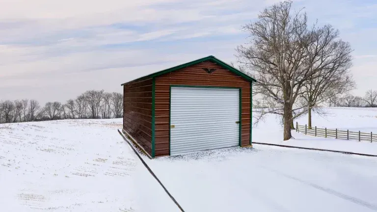 A metal garage with a green roof is sitting in the middle of a snowy field.