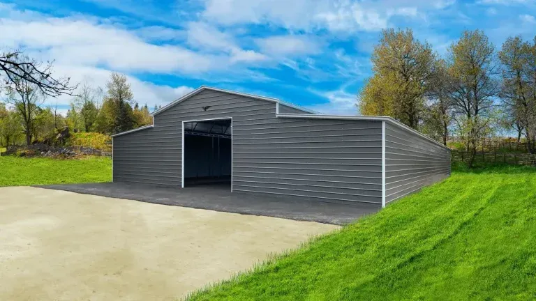 A large metal barn is sitting on top of a lush green hillside.