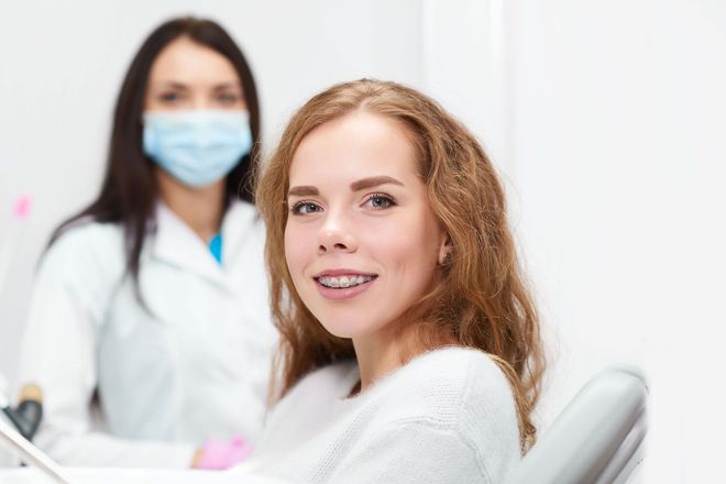 Woman smiling in a dental chair with a masked dentist in the background