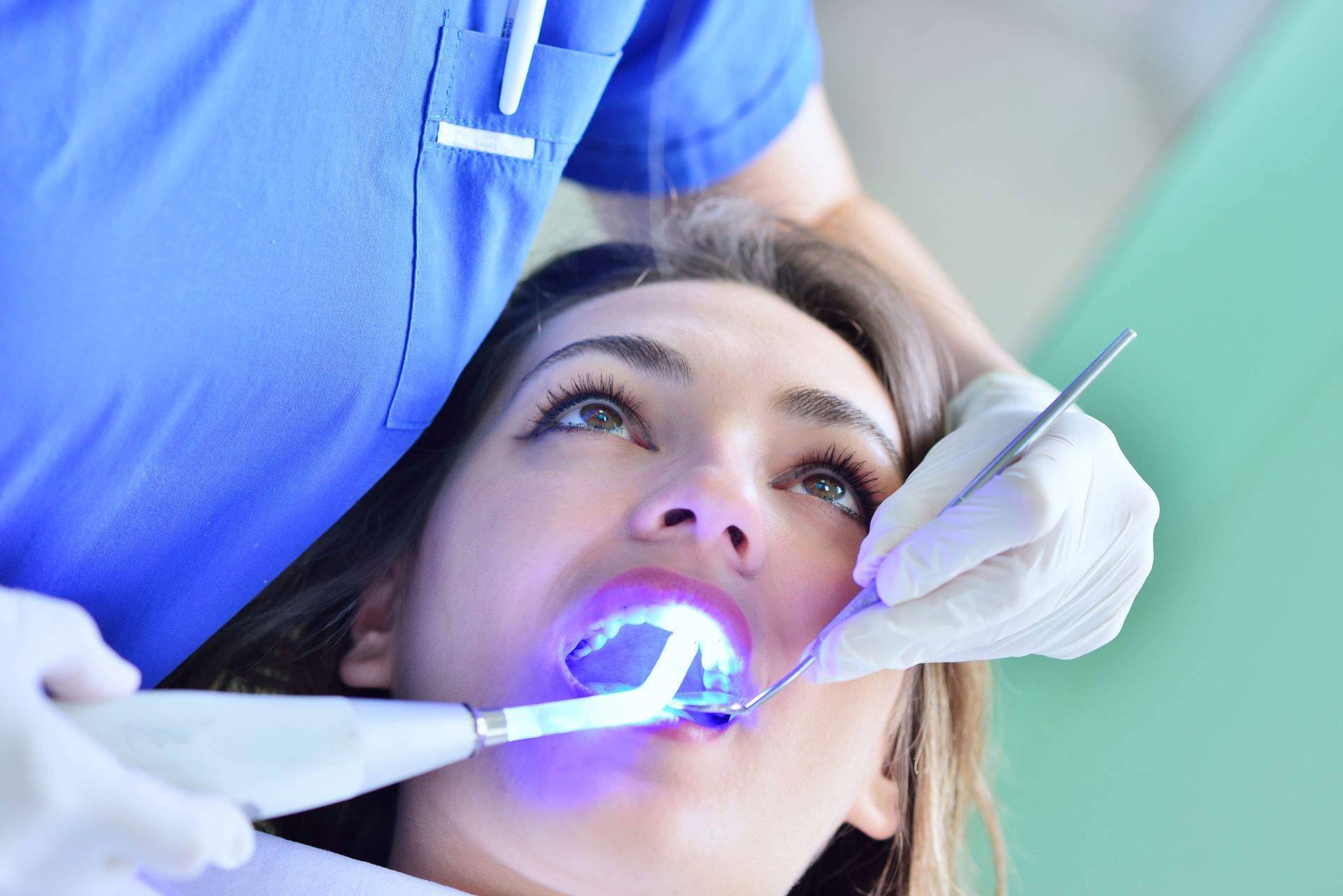 A dentist uses a blue UV curing light on a patient's teeth during a dental procedure.