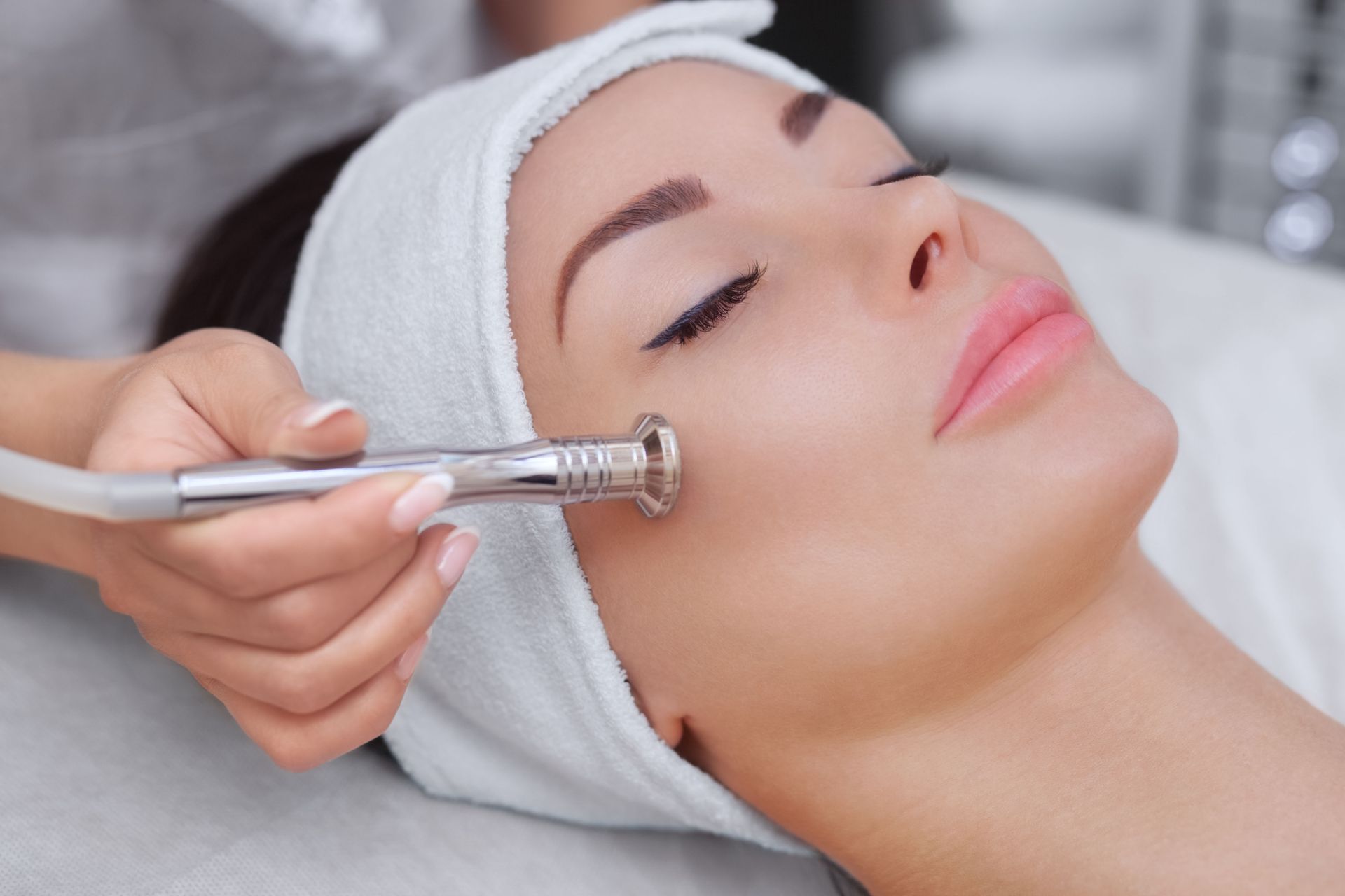 A person receives a microdermabrasion facial treatment in a spa, with a handheld device gently touching their cheek.