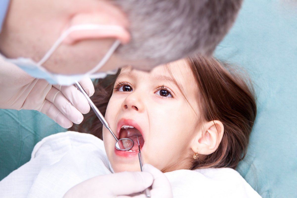Dentist examining a child’s open mouth with dental tools in a clinic