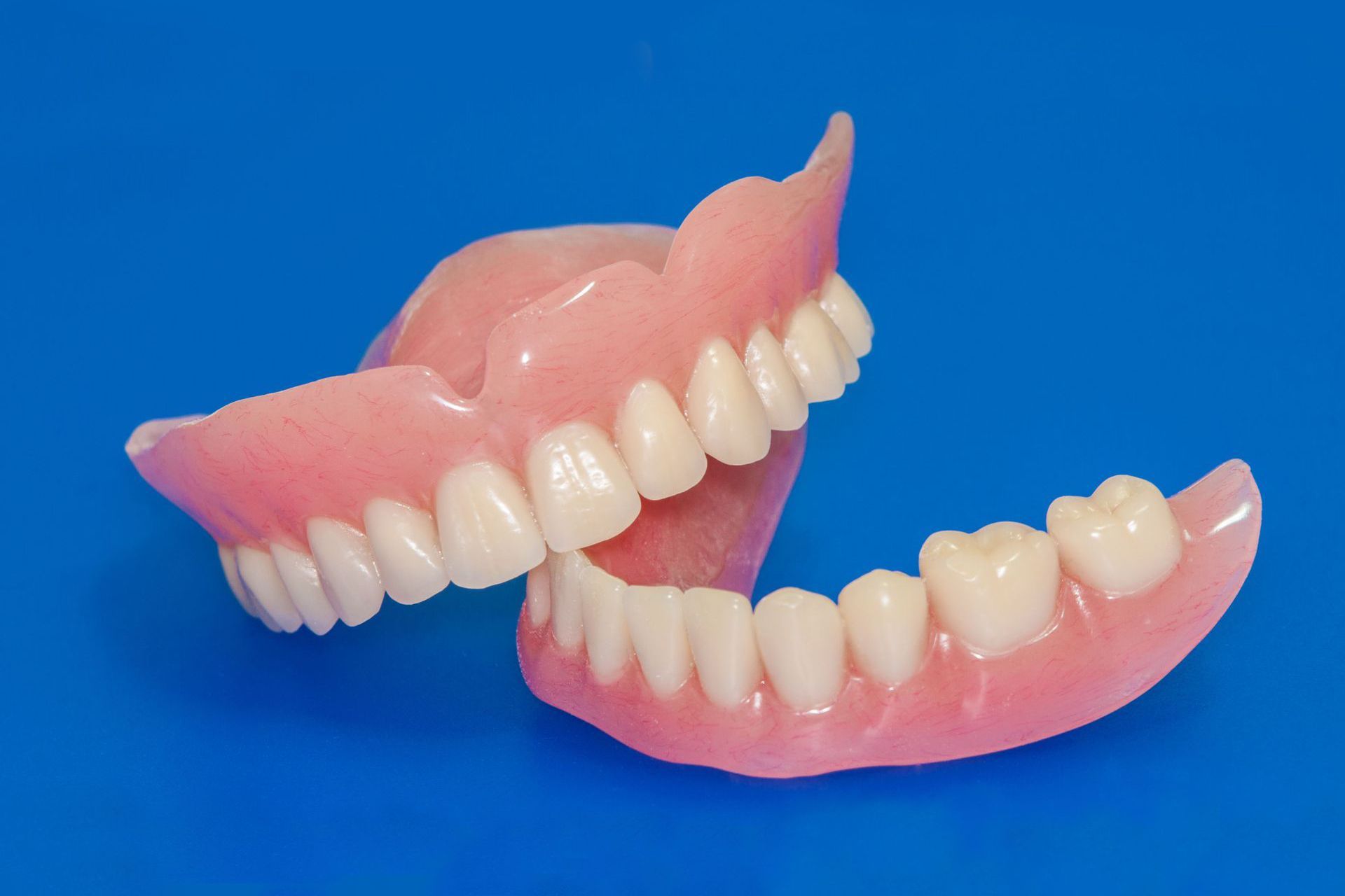 Two pink and white dental dentures on a bright blue background