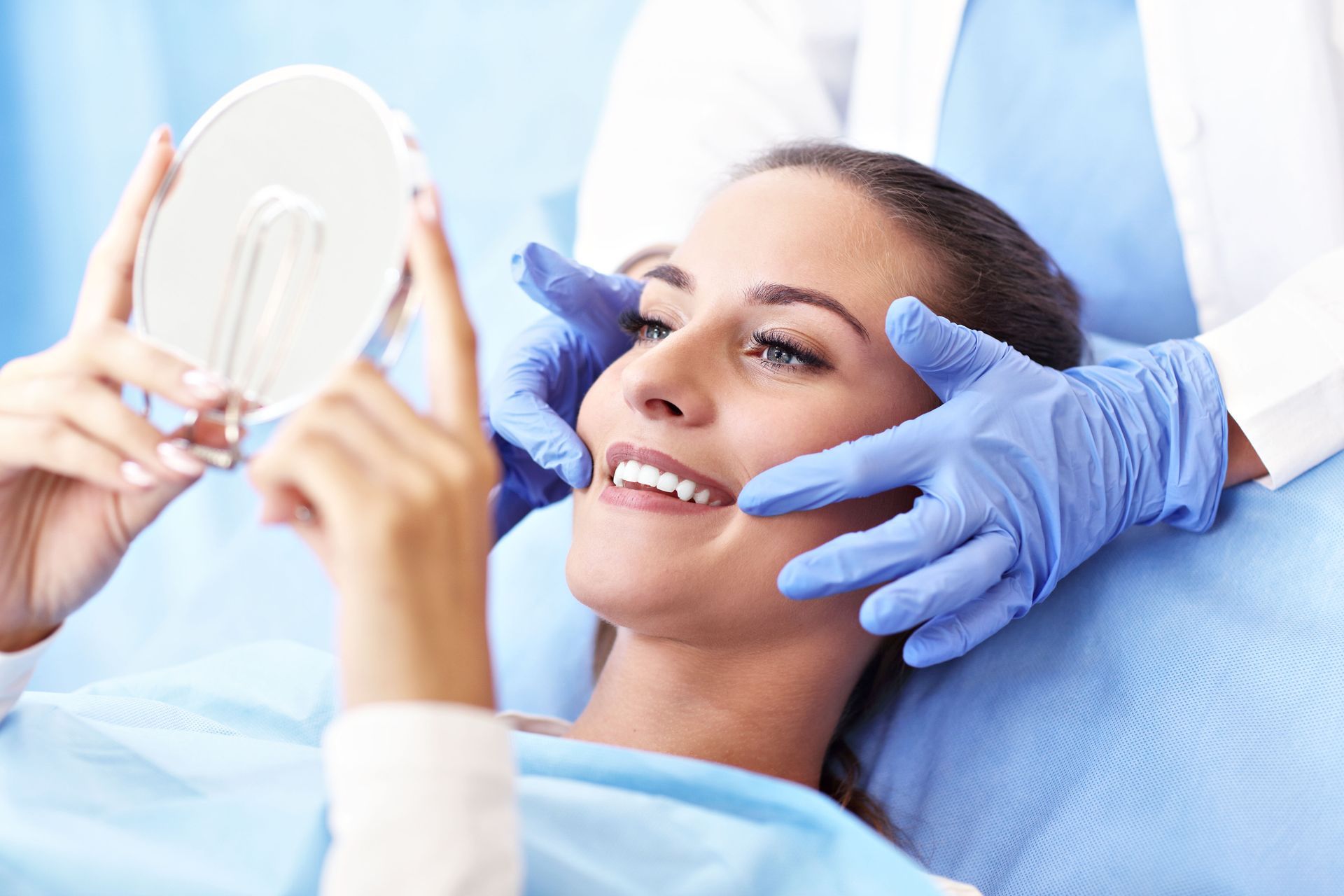 Woman smiling as she examines her face with a small mirror