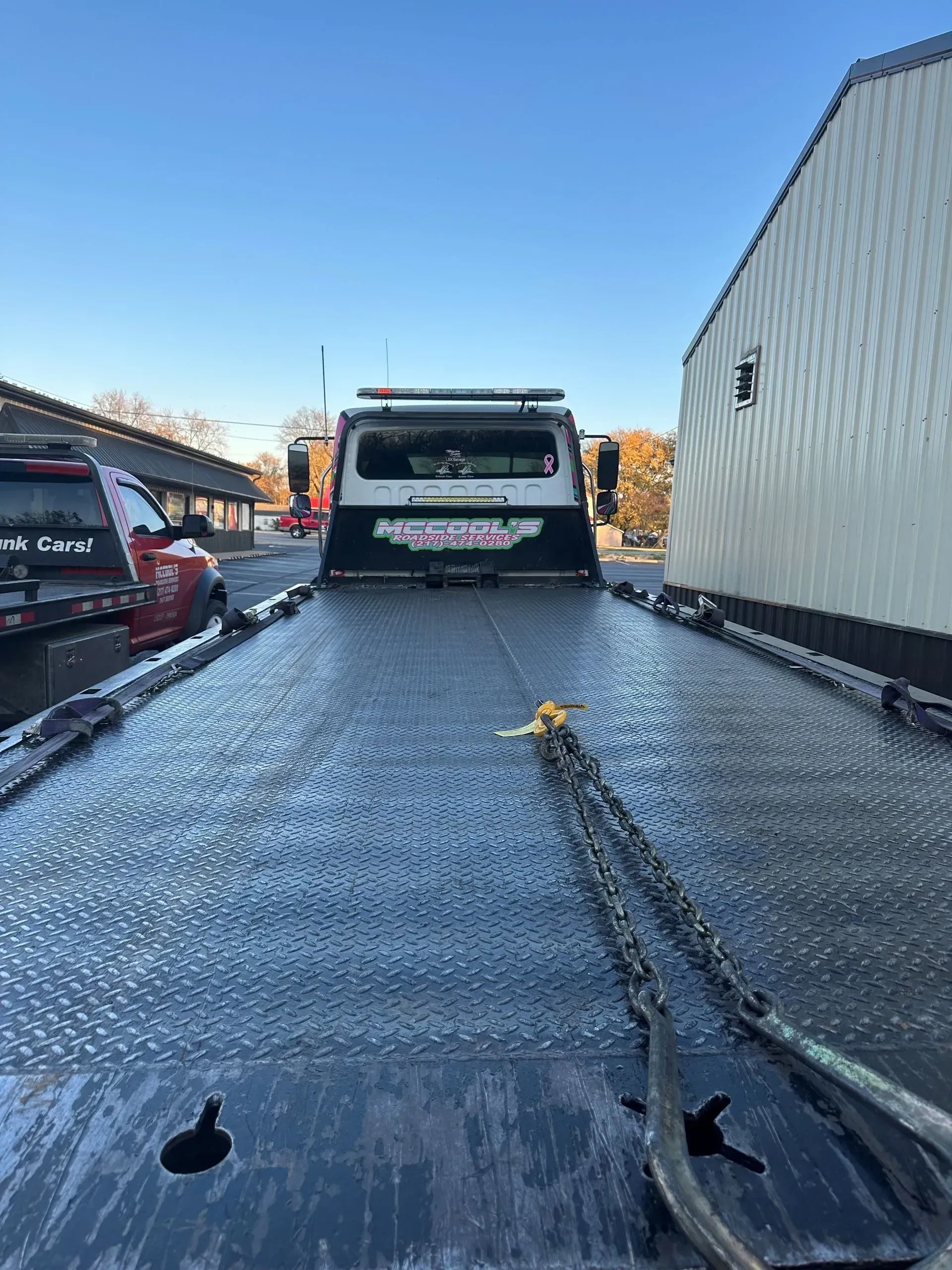 Tow truck bed with chains, ready to transport a vehicle outdoors under a blue sky.