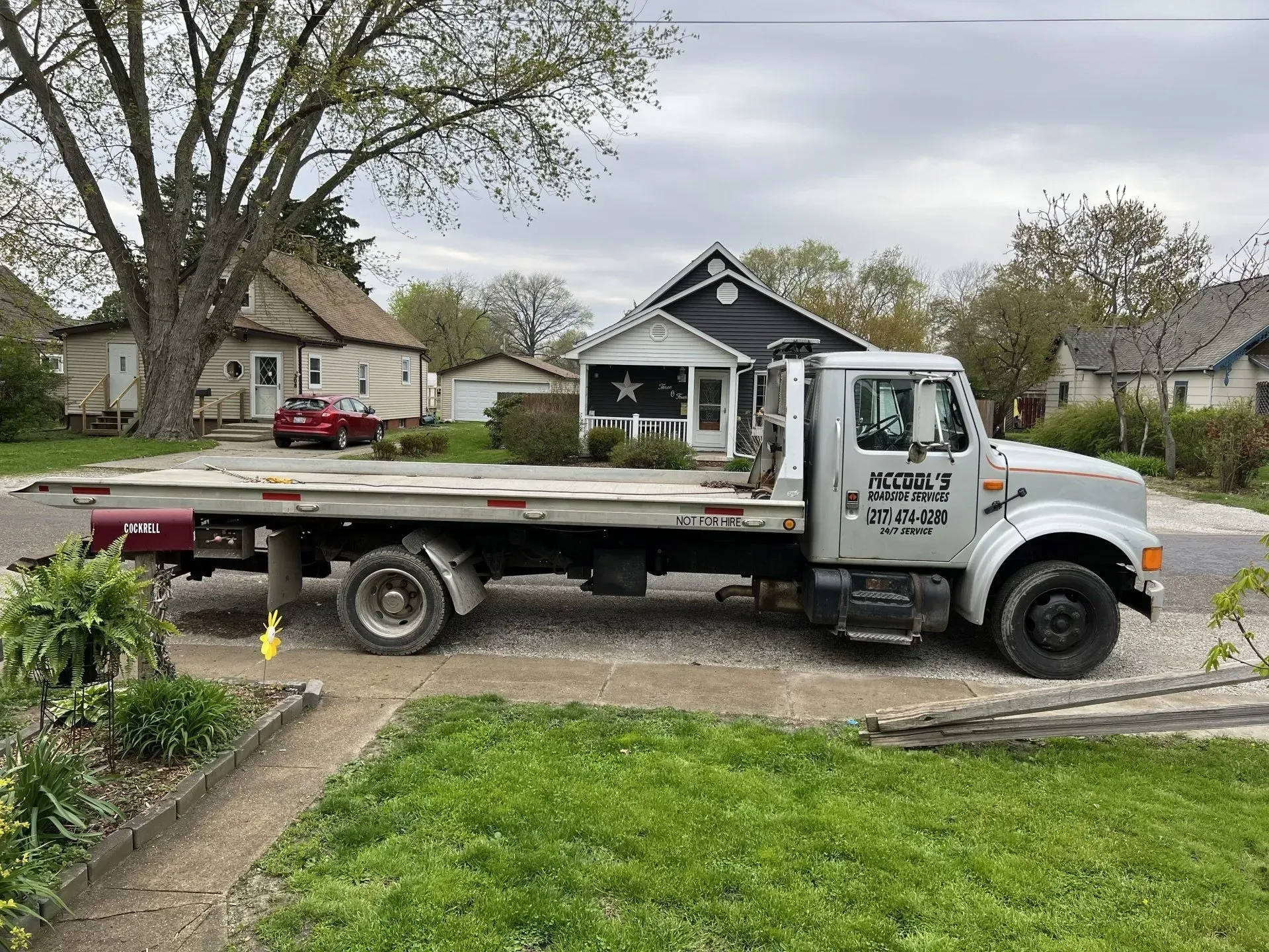 Tow truck parked on a residential street in front of houses; cloudy sky.