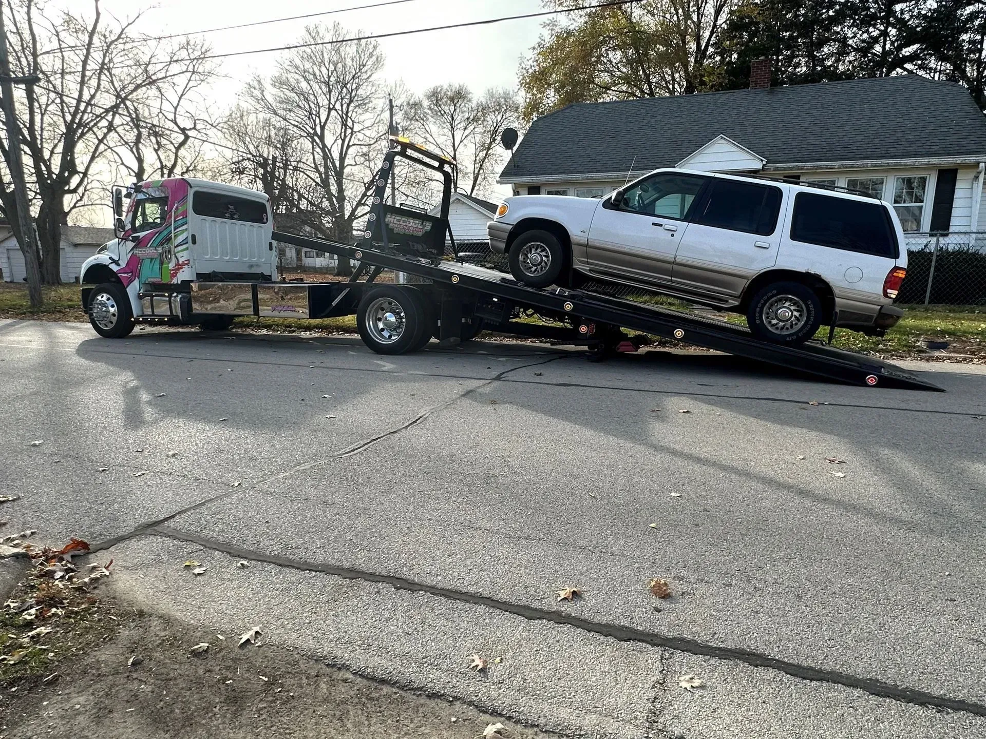 Tow truck with a white SUV on its ramp on a street in front of a house.
