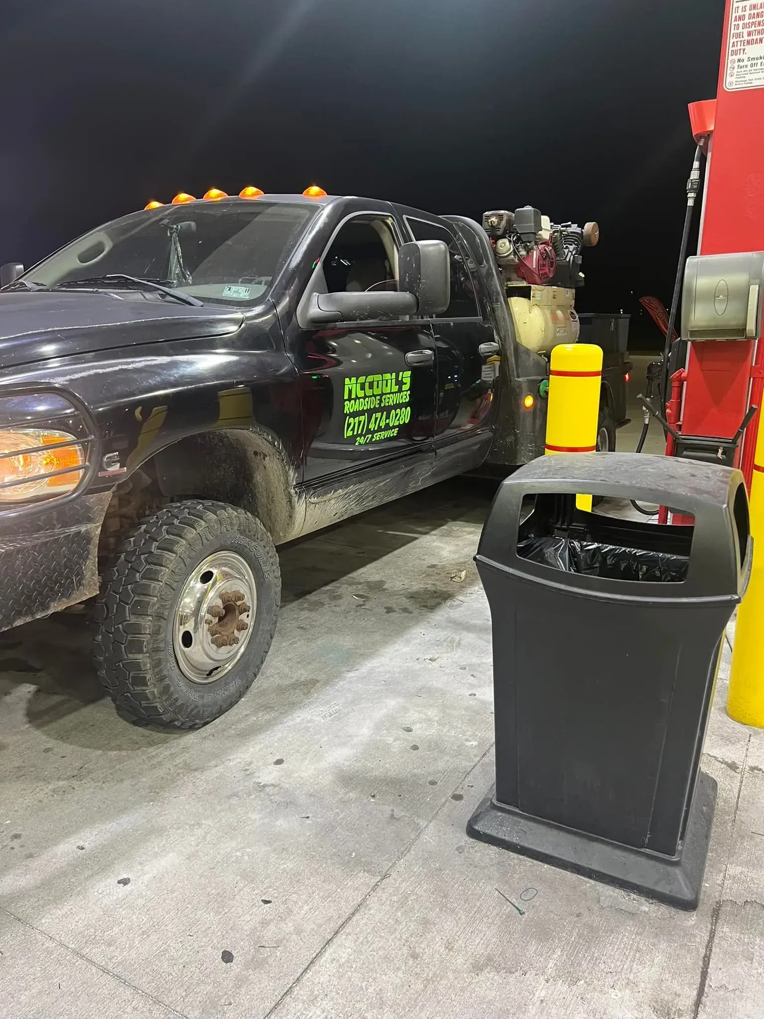 Dark truck at a gas pump next to a trash can; night setting.