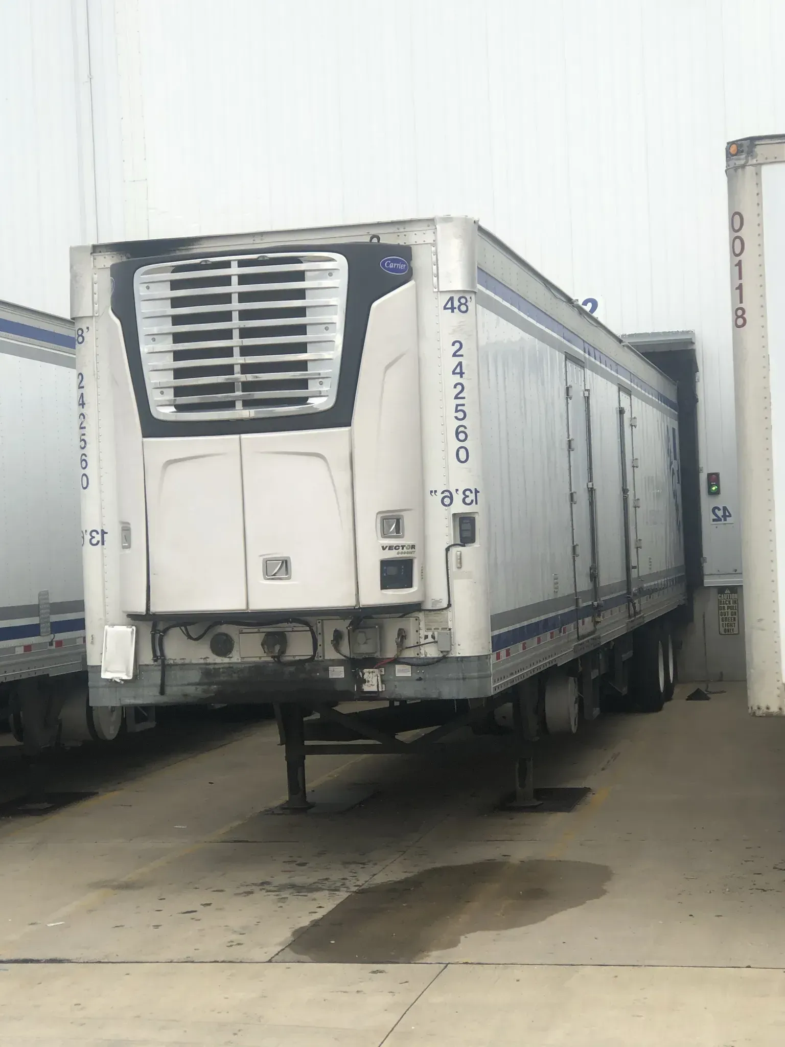 White refrigerated semi-trailer parked at loading dock, with cooling unit on front.