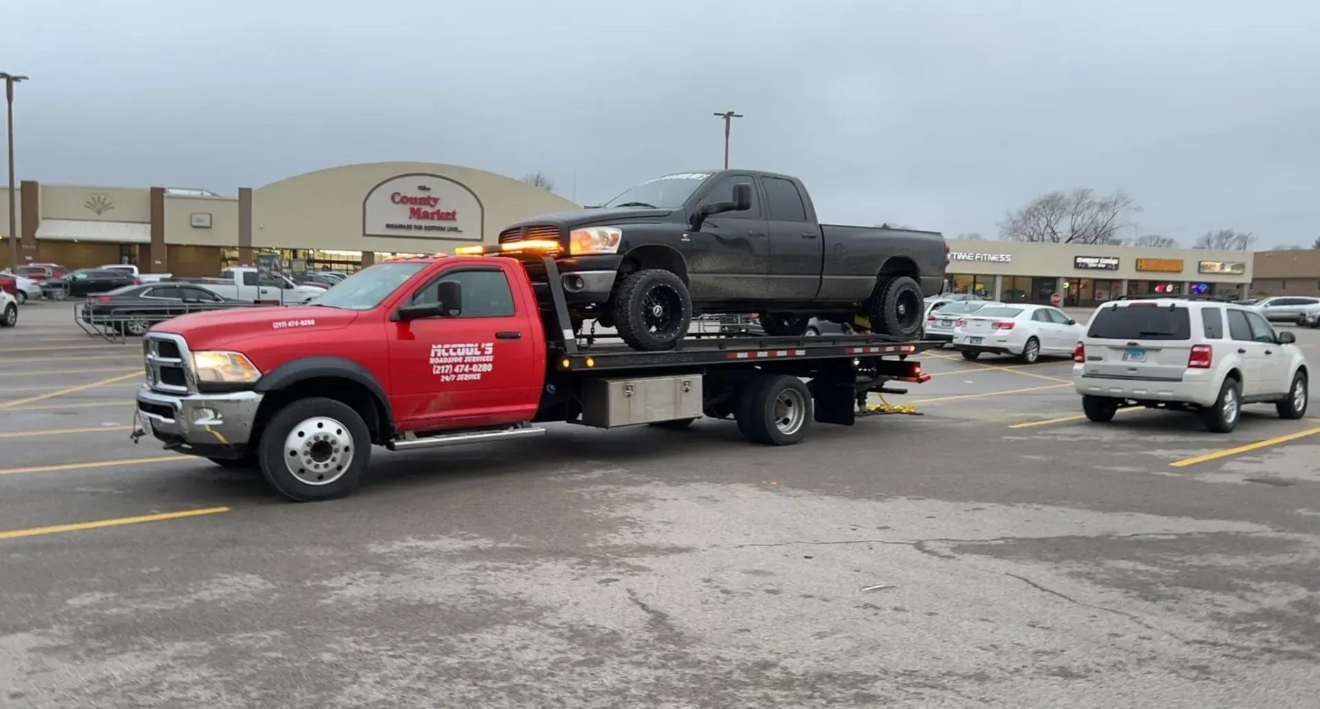 Red tow truck carrying a black pickup truck in a parking lot.