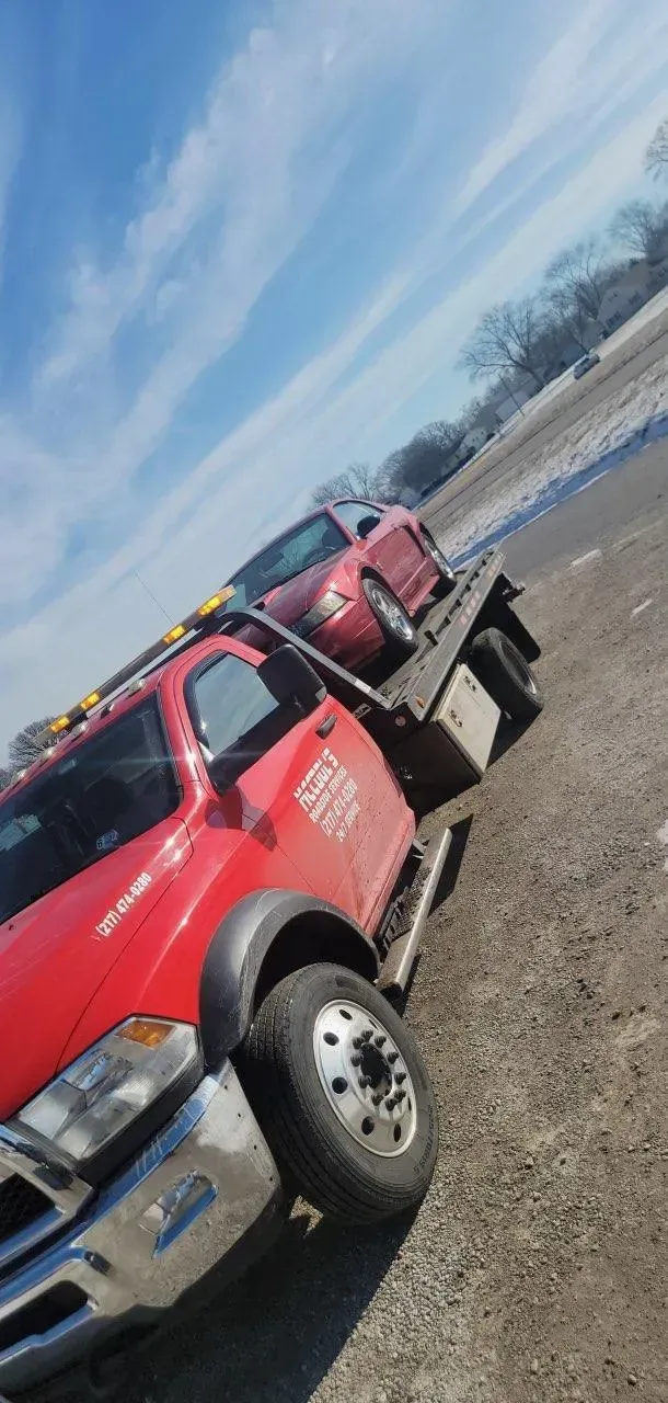 Red tow truck hauling a red car under a partly cloudy sky.