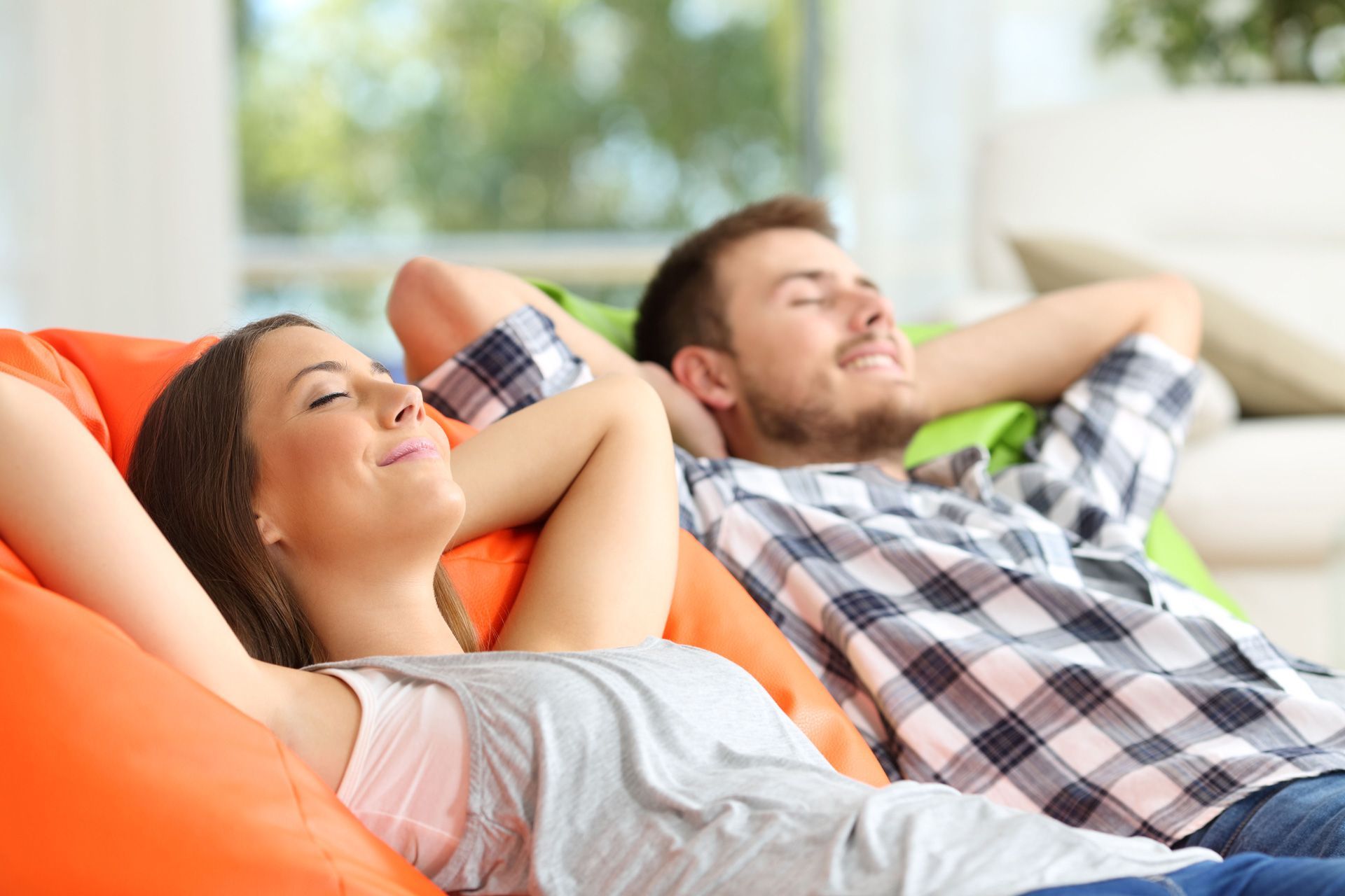 Woman and man relaxing on colorful beanbag chairs, eyes closed, indoors.