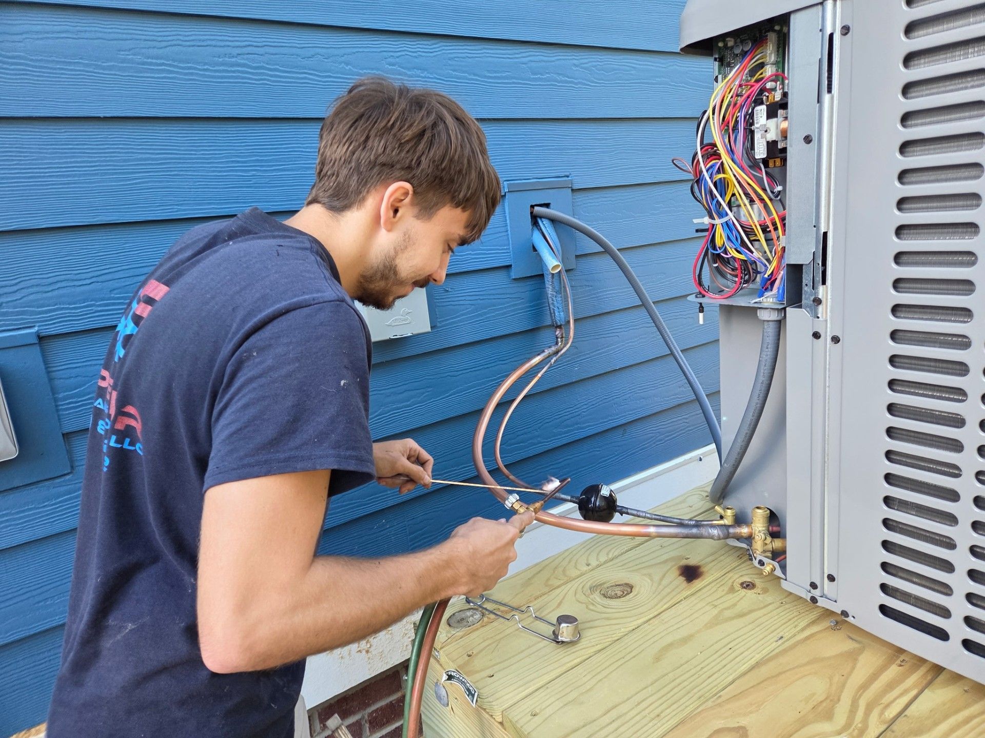 HVAC technician working on an air conditioning unit outside a blue-sided building.