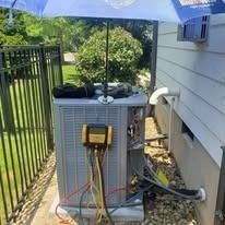 Air conditioning unit being serviced outdoors under a blue umbrella, with tools attached.