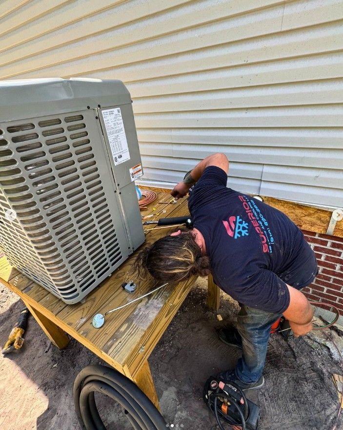 HVAC technician working on an air conditioning unit on a wooden table outdoors.