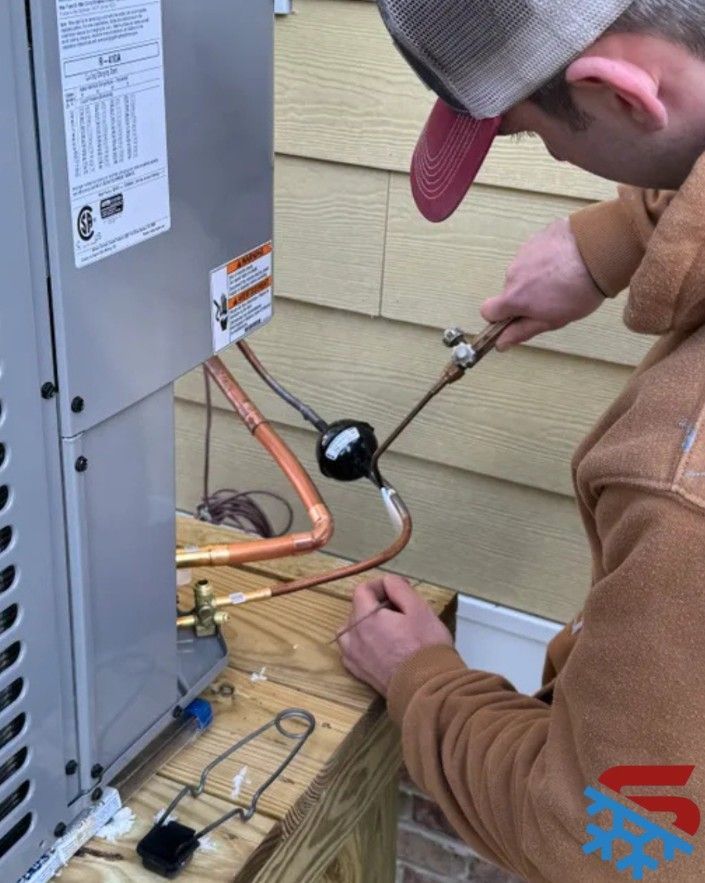 HVAC technician brazing copper pipes on an air conditioning unit outside a building.