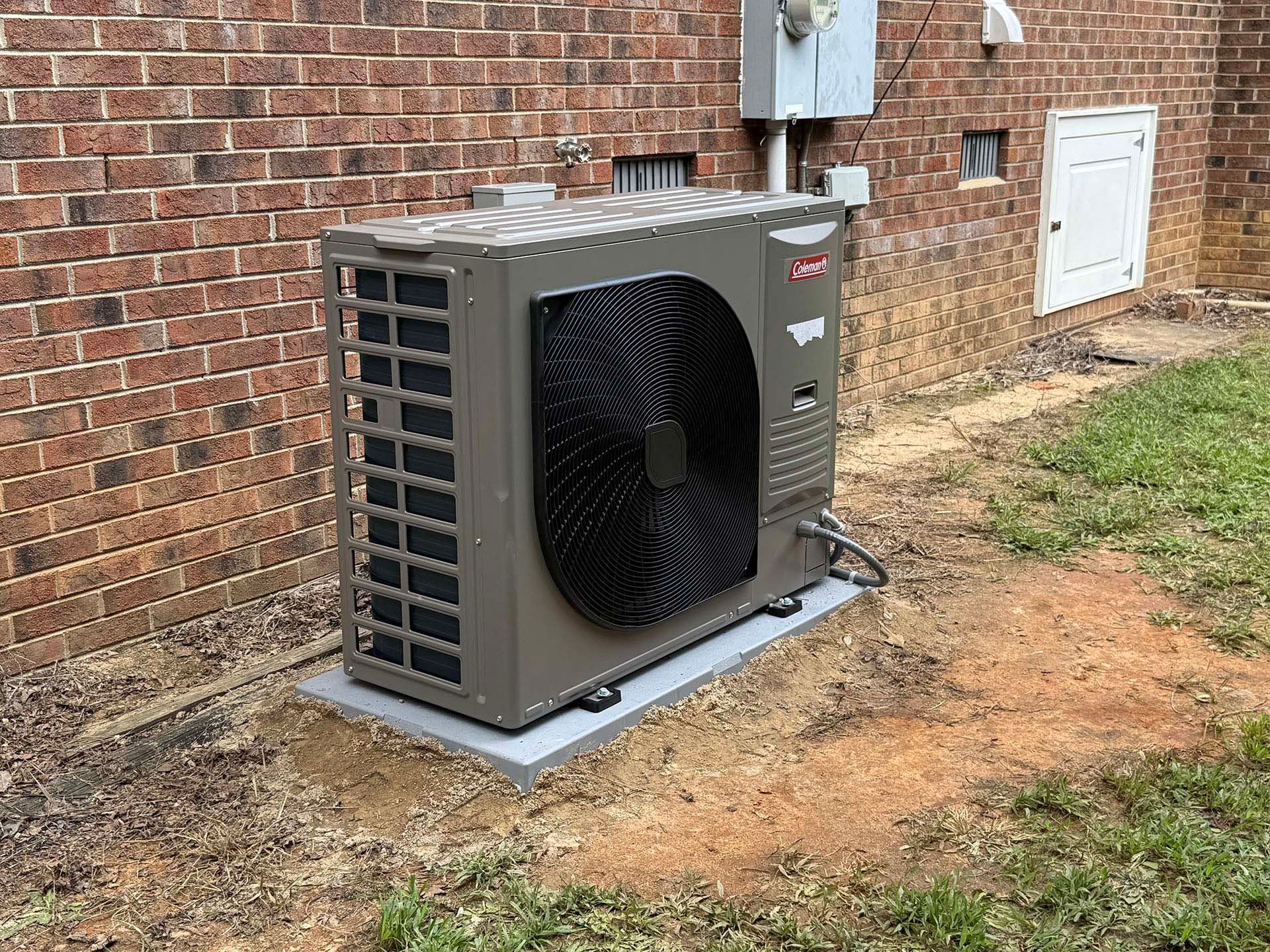 Exterior air conditioning unit on a concrete pad next to a brick building.