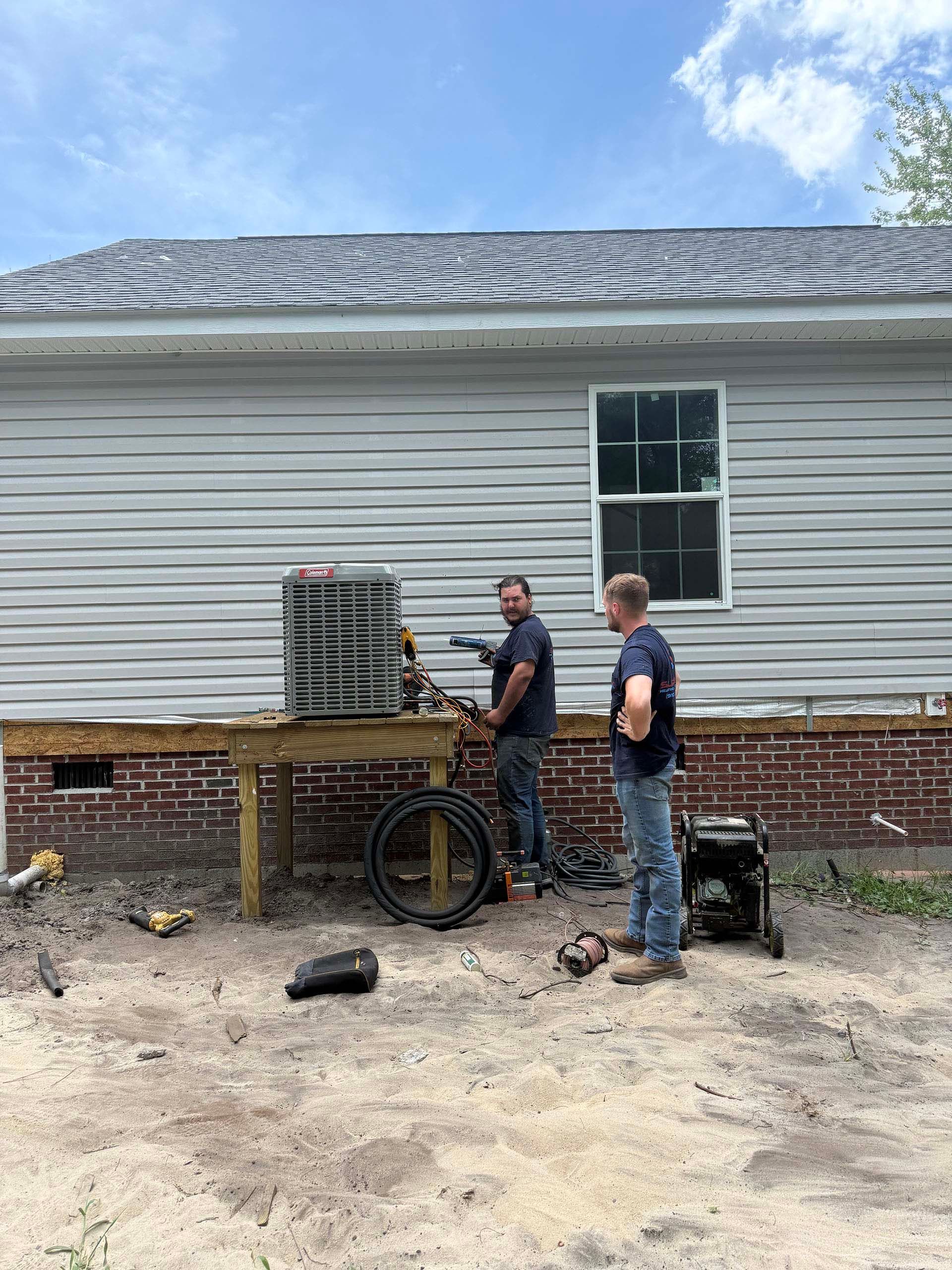Two men install an air conditioning unit outside a house.