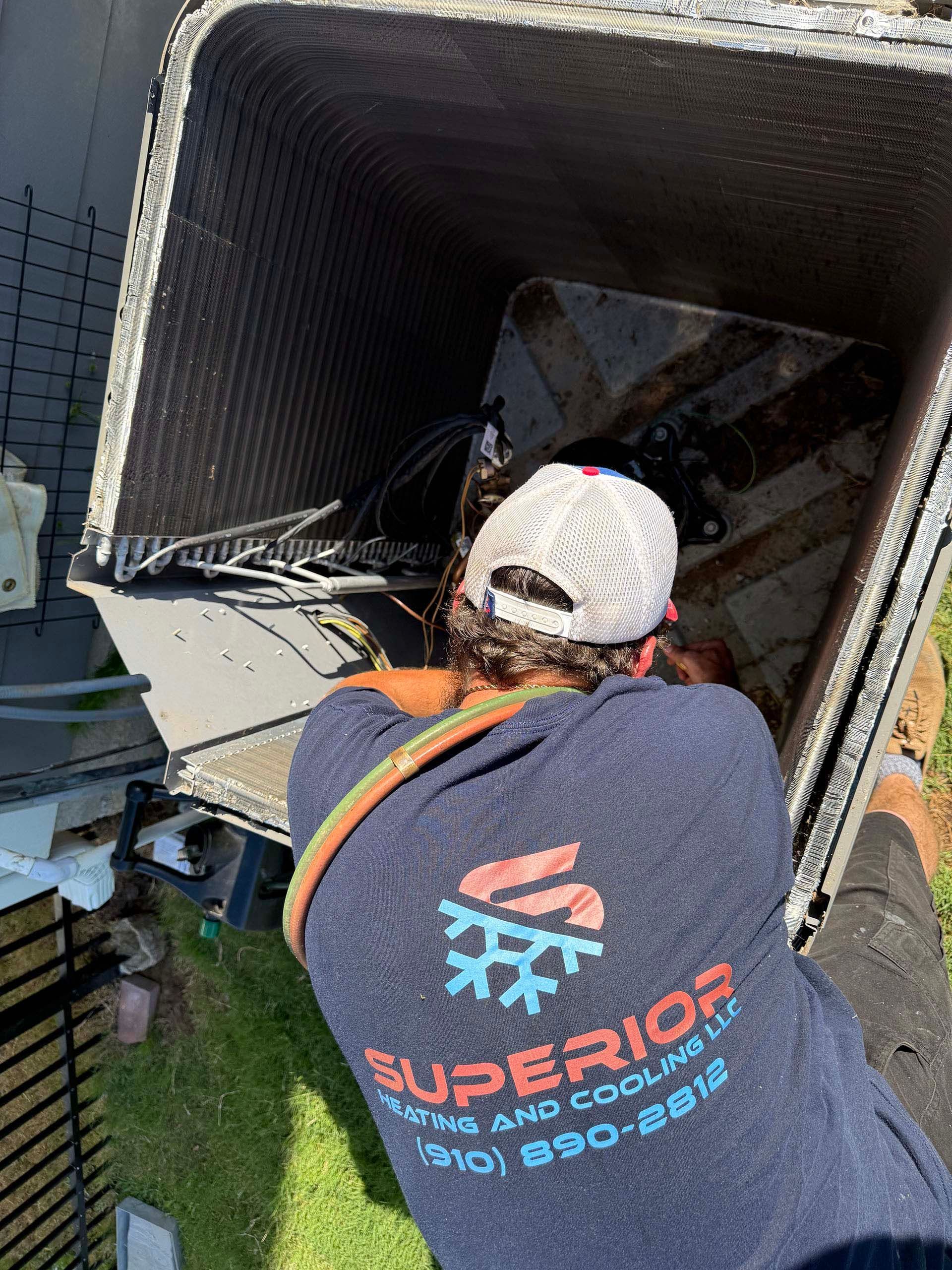 HVAC technician working inside an air conditioning unit; the worker wears a cap and a company shirt.