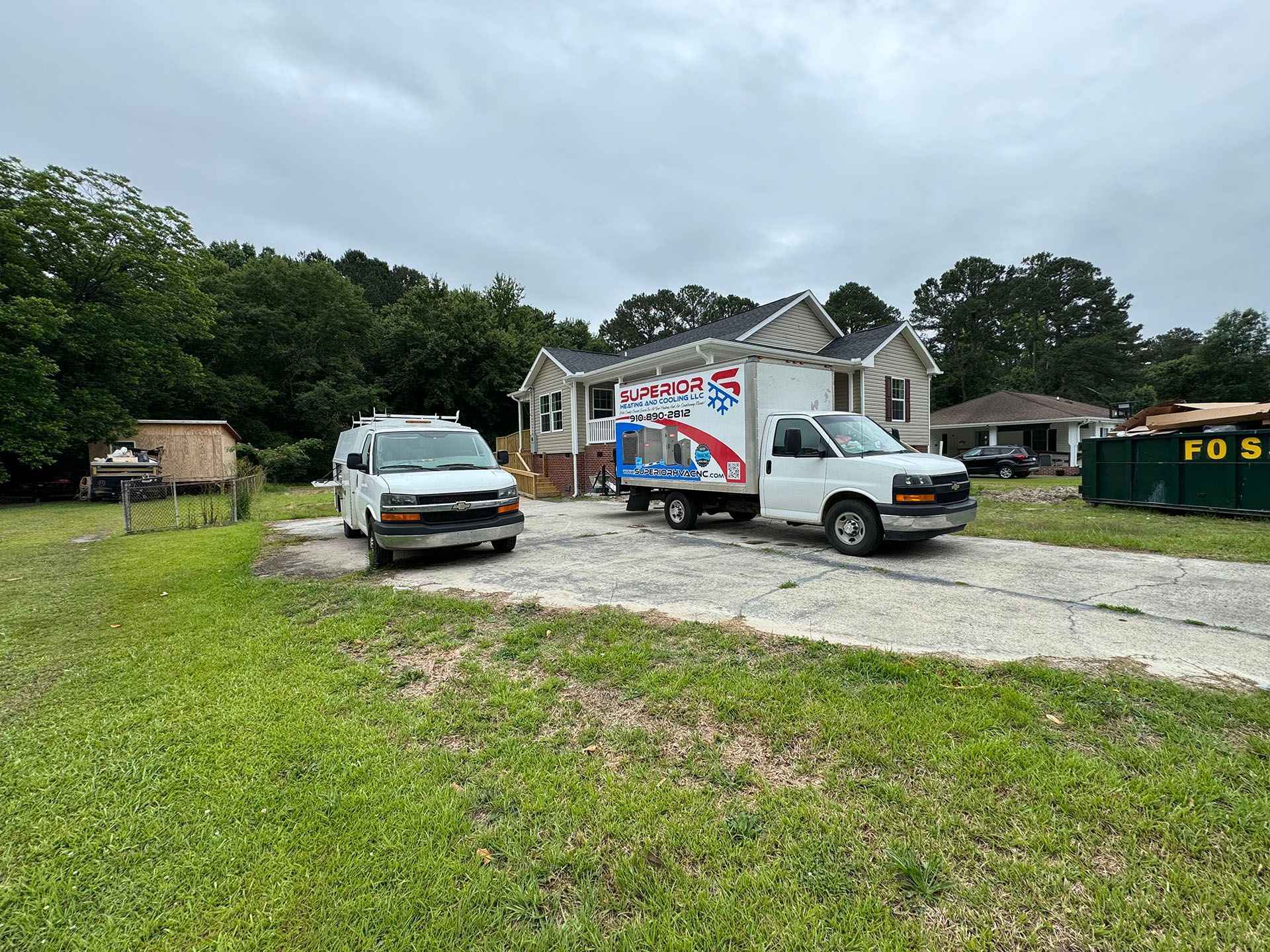 A small house with two work trucks in the driveway. The sky is overcast.