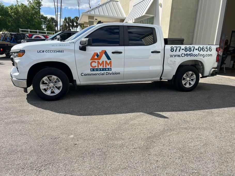 White CMM roofing truck parked on asphalt; business logo and phone number displayed.