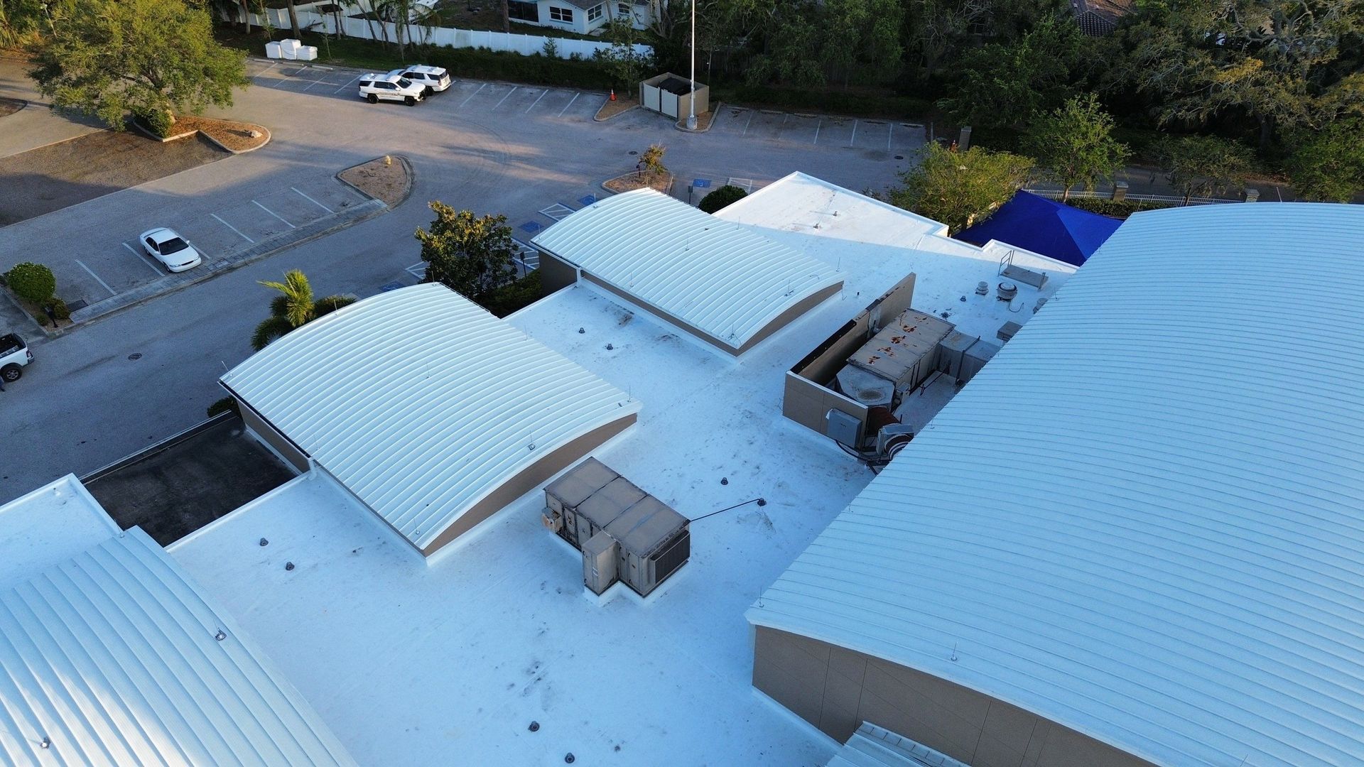 Aerial view of a building complex with light blue roofs and a parking lot nearby.