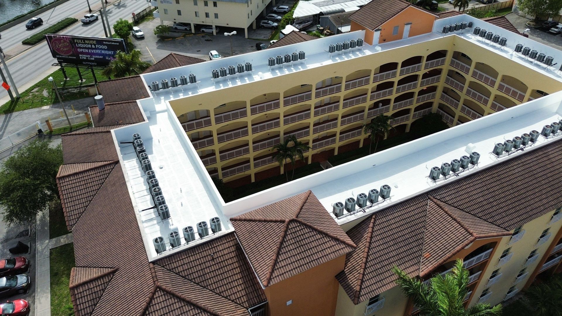 Aerial view of a yellow apartment building with white roofs and red-tiled surroundings.