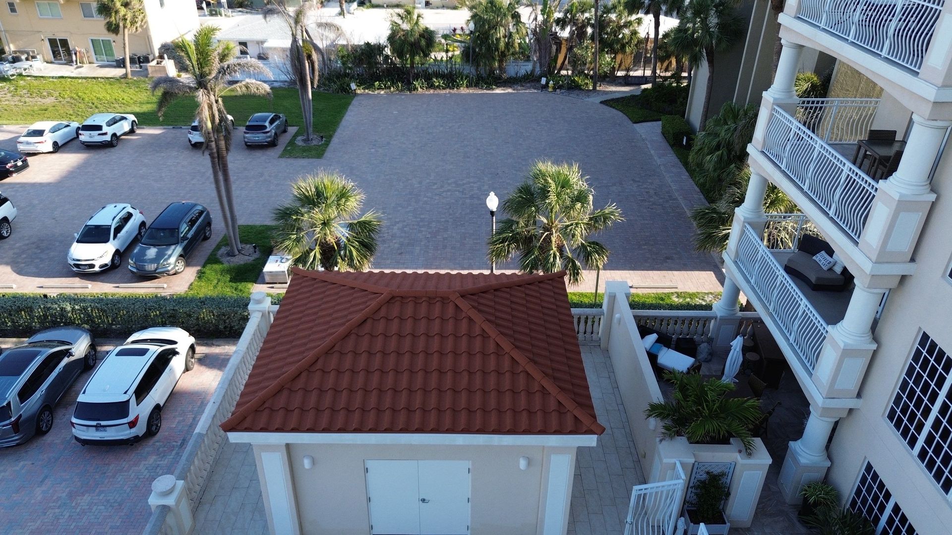 View from balcony over a parking lot, trees, and a small red-roofed building beside an apartment complex