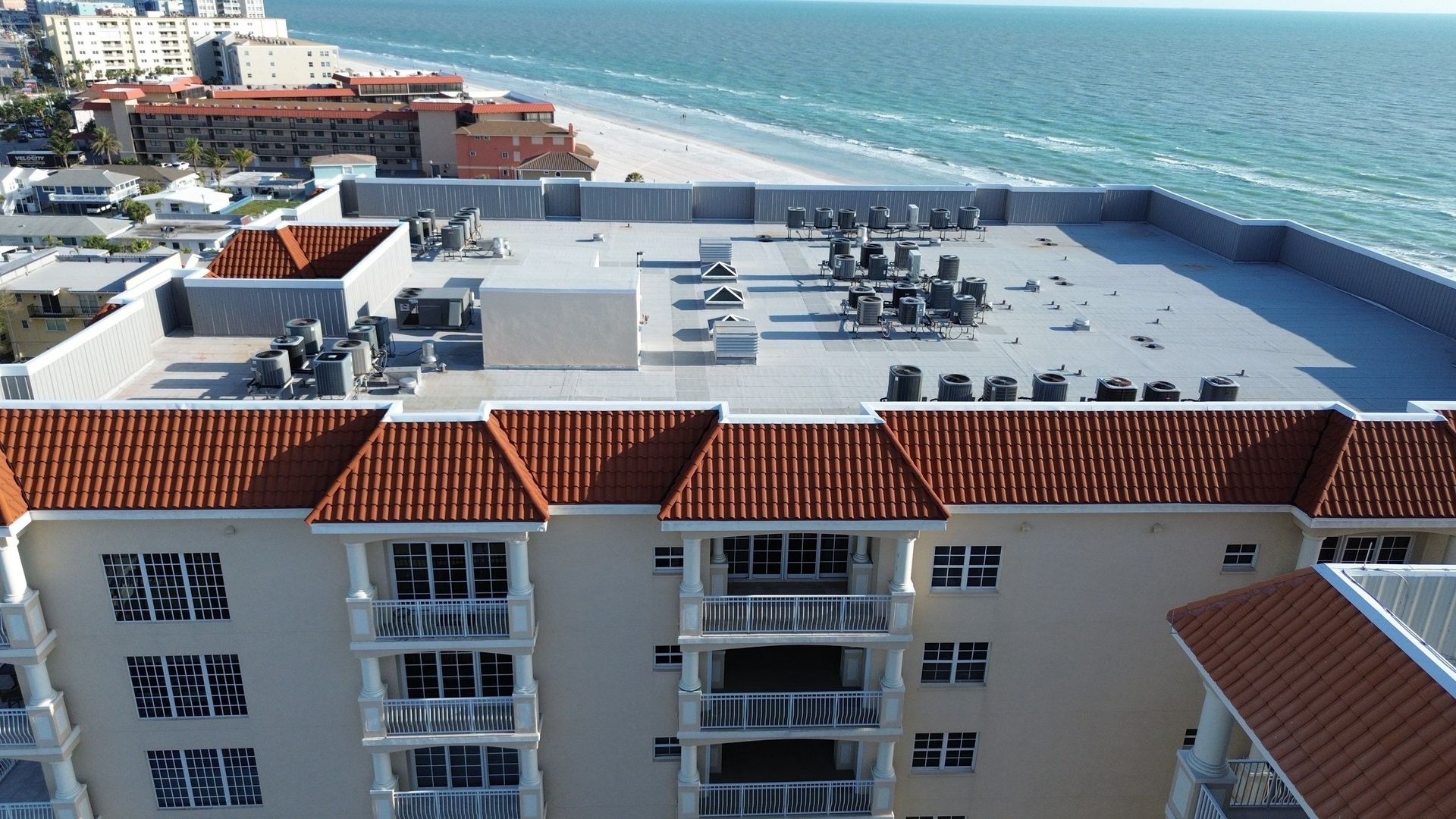 White-roofed seaside hotel buildings beside turquoise ocean under a clear sky