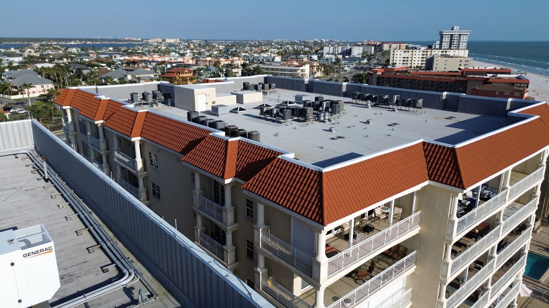 Aerial view of a modern apartment complex with red-tiled roofs in a coastal city.