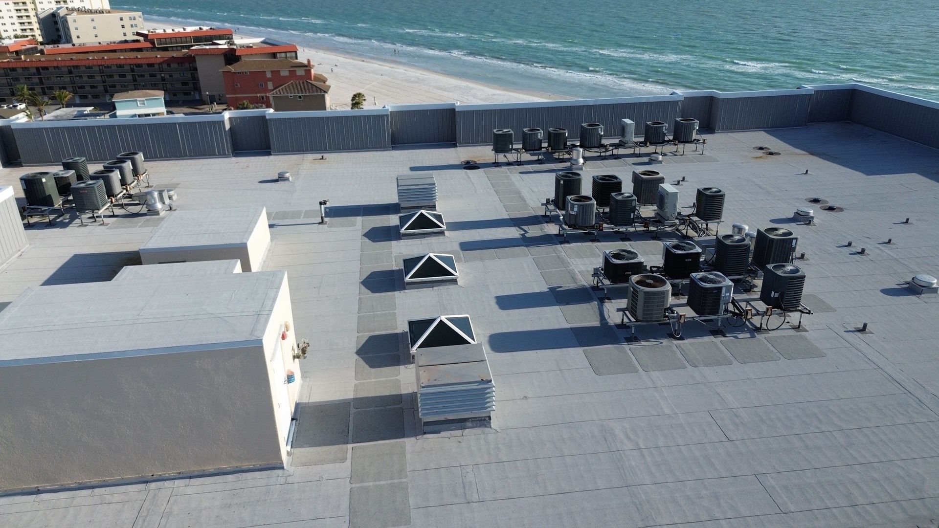 Rooftop HVAC units and vents on a flat gray roof overlooking the ocean
