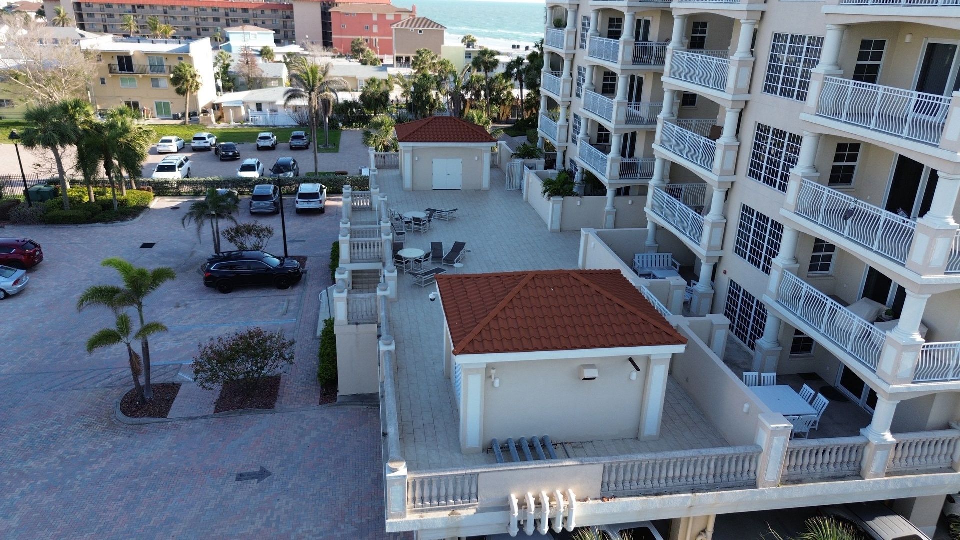 Apartment complex courtyard with parked cars, palm trees, and a small white building with a red roof