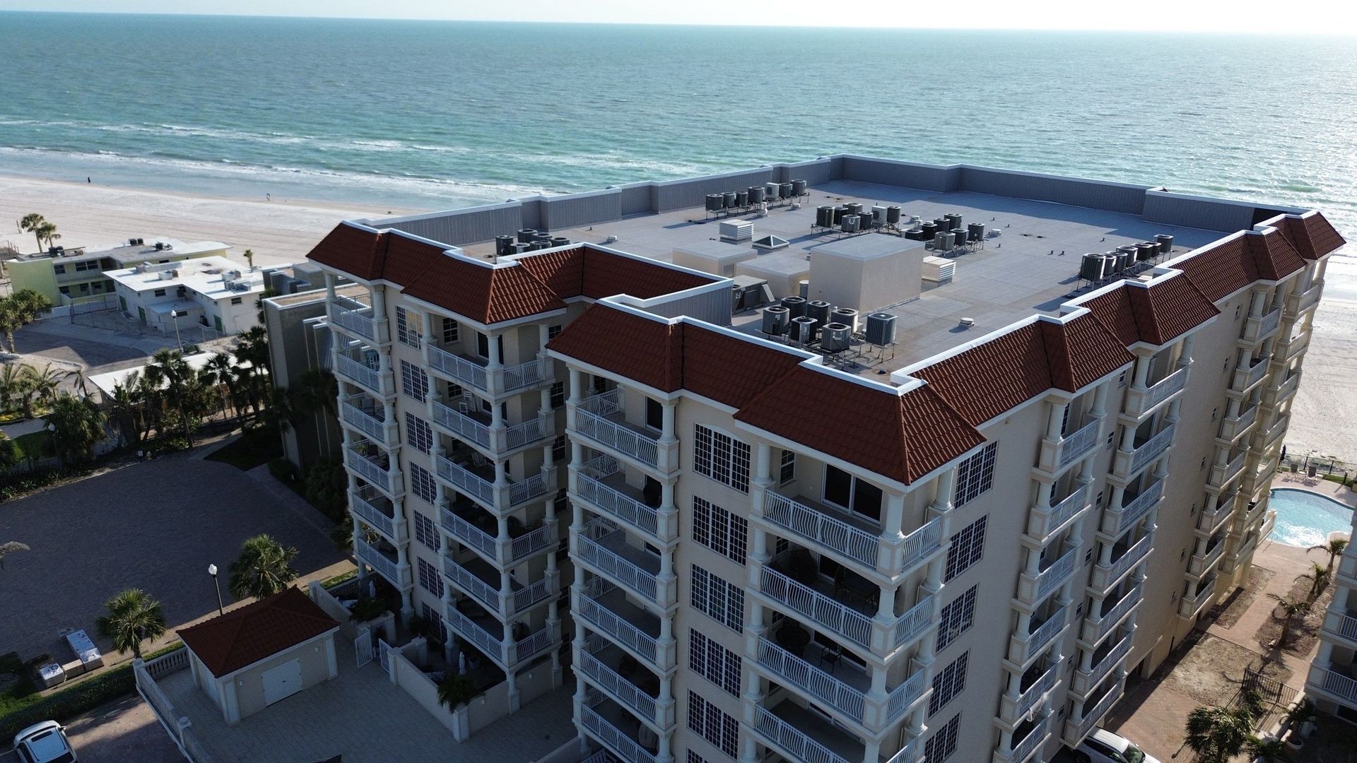Aerial view of a beachfront condo building beside the ocean with a rooftop deck and parking area