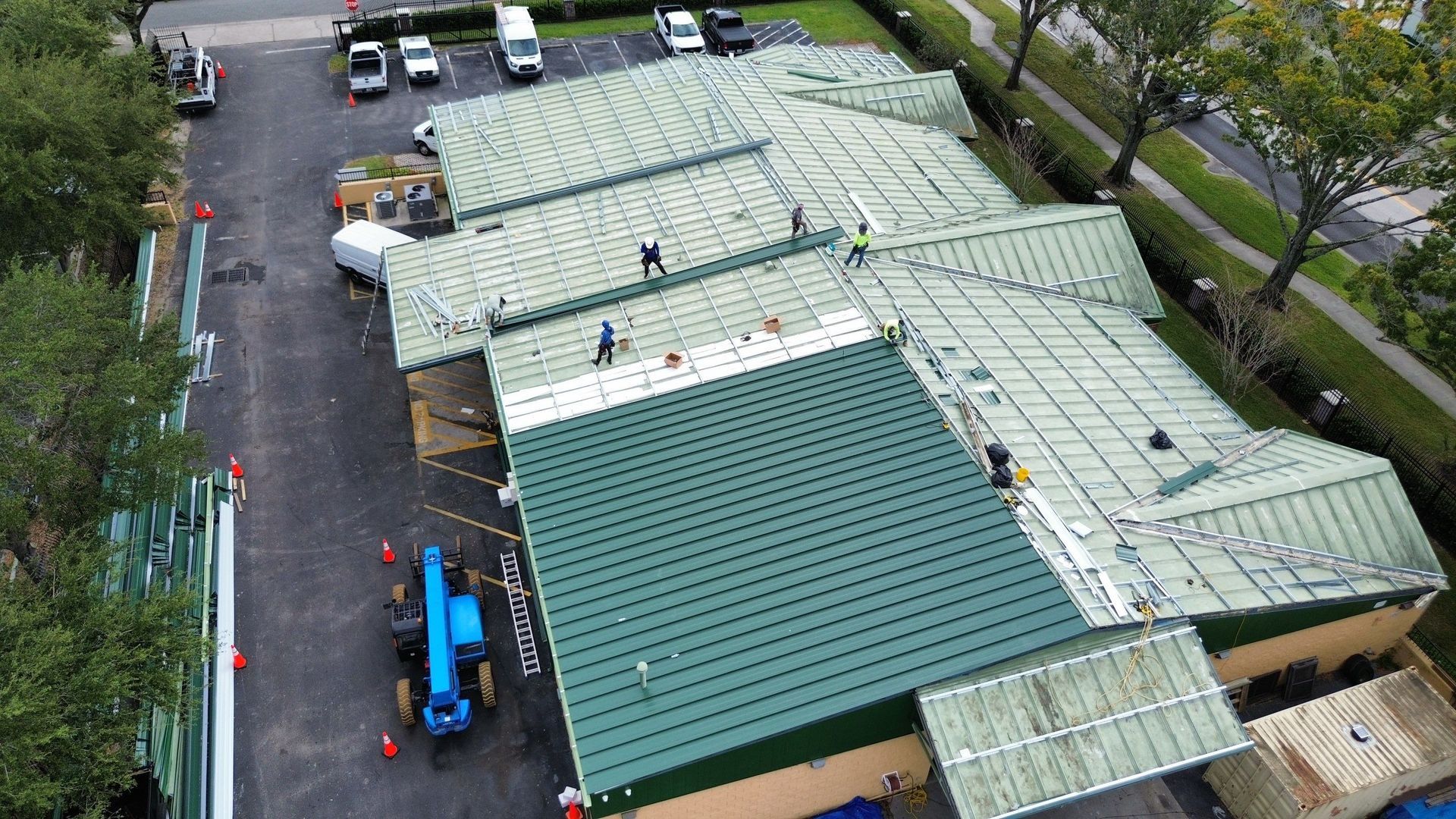 Aerial view of a large building with green roofs beside a wet parking lot and trees.