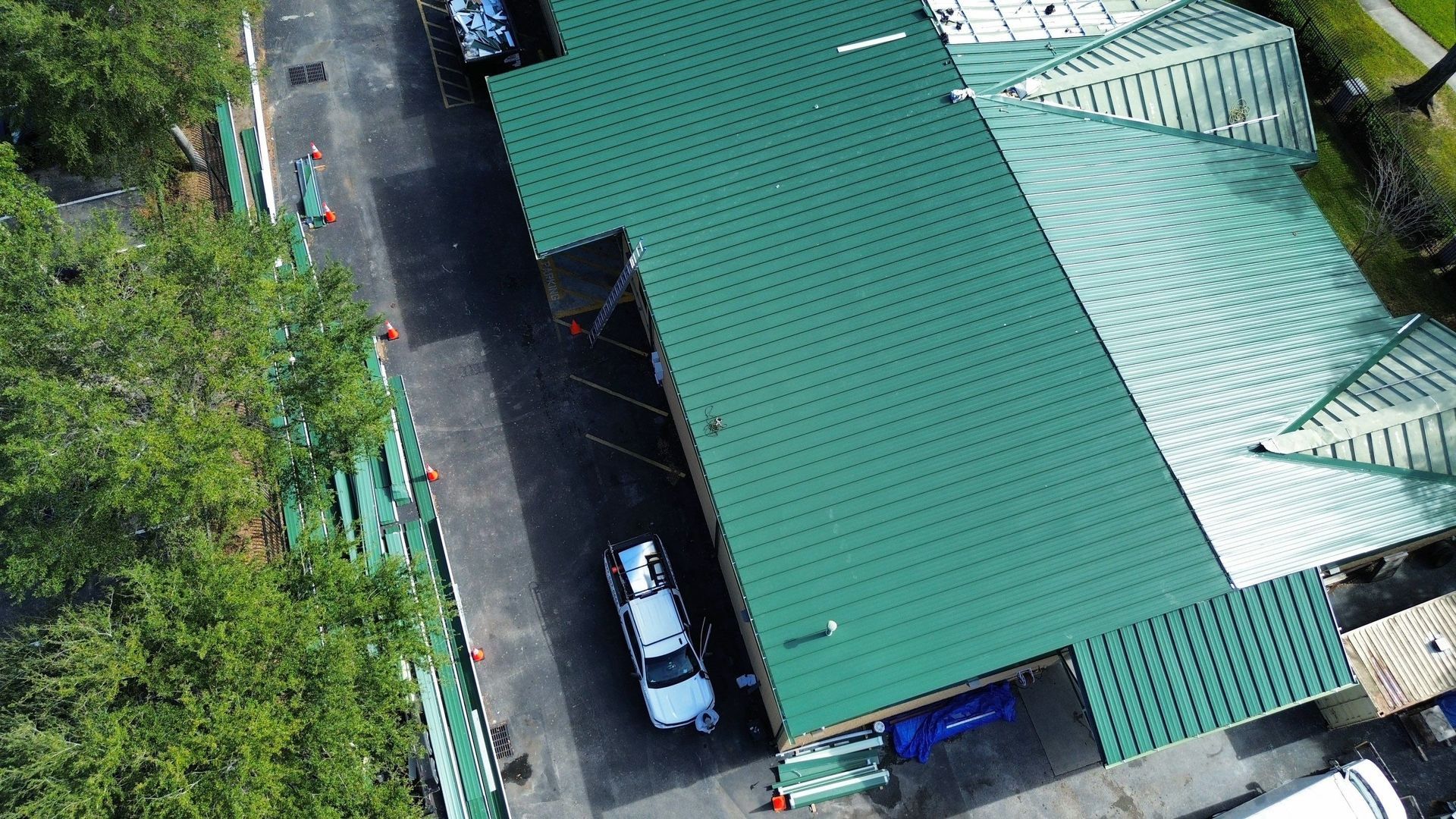 Aerial view of a green-roofed building beside a road, with parked vehicles and trees nearby