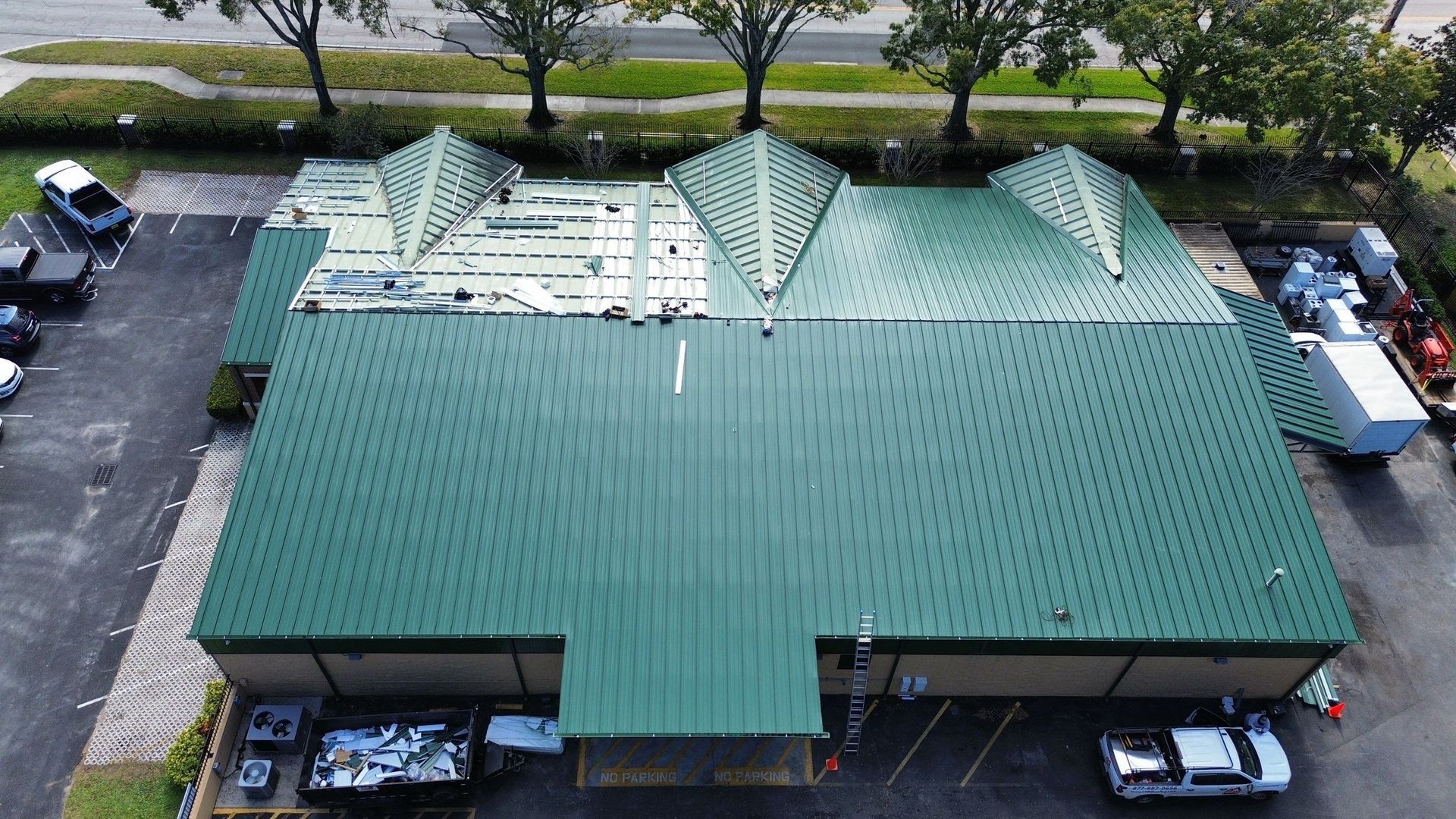Aerial view of a large green-roofed building with parking lots and trees around it.