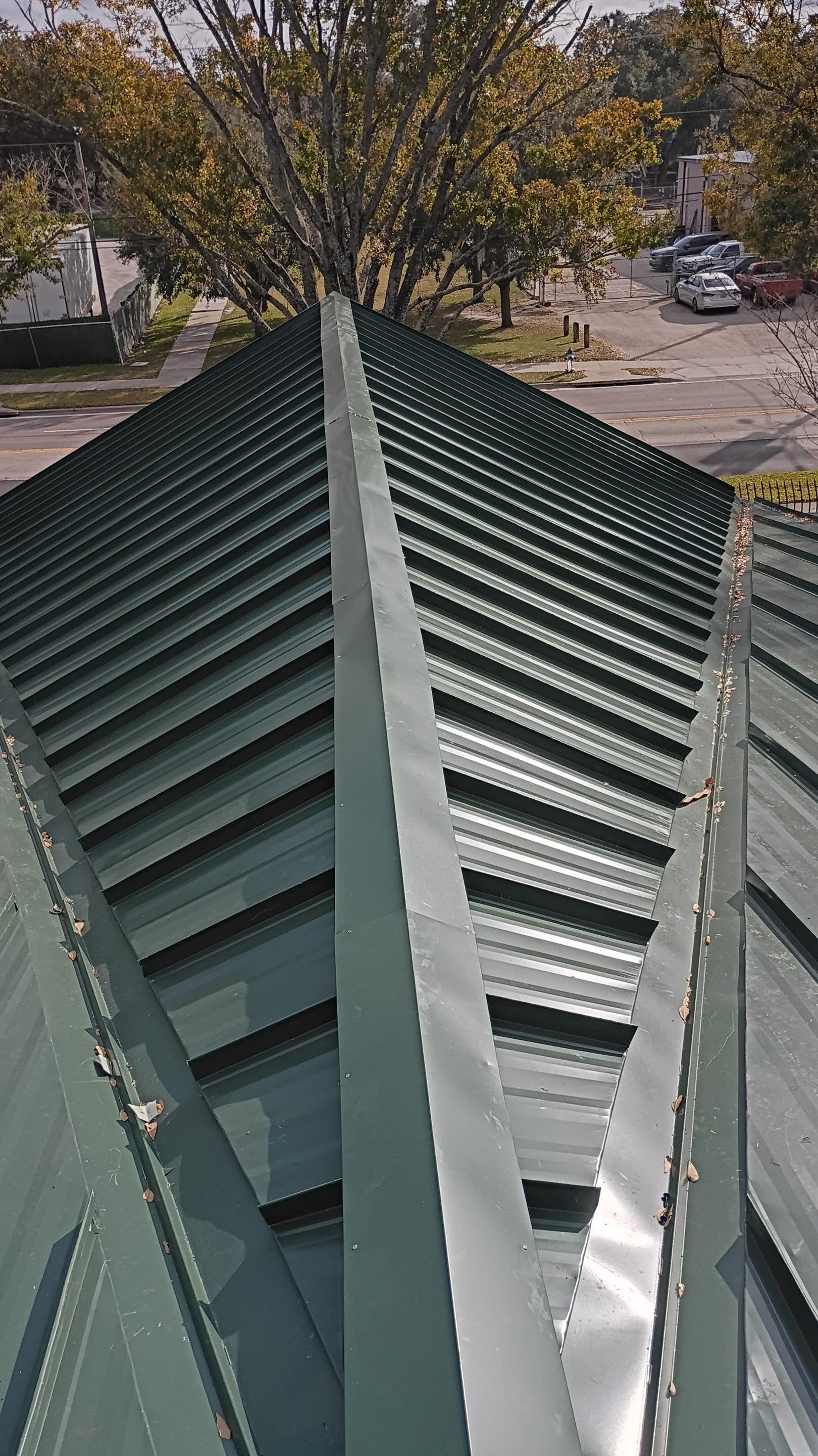 Green metal roof ridge with trees and parked cars visible below
