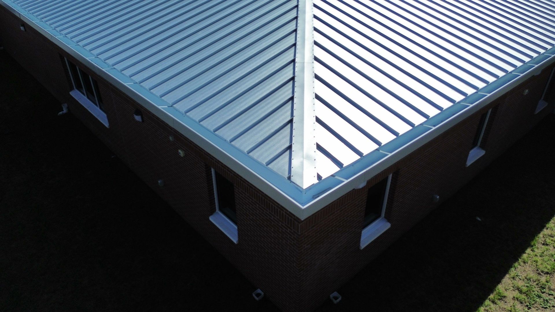 Corner of a building with a blue metal roof and brick walls viewed from above