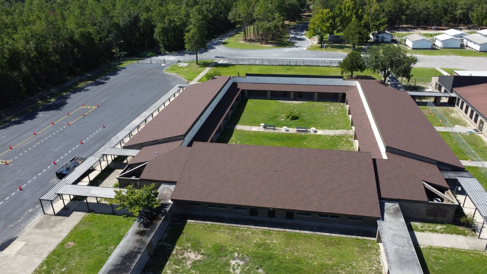Aerial view of a flat-roofed building with a central courtyard, surrounded by trees and parking lots.