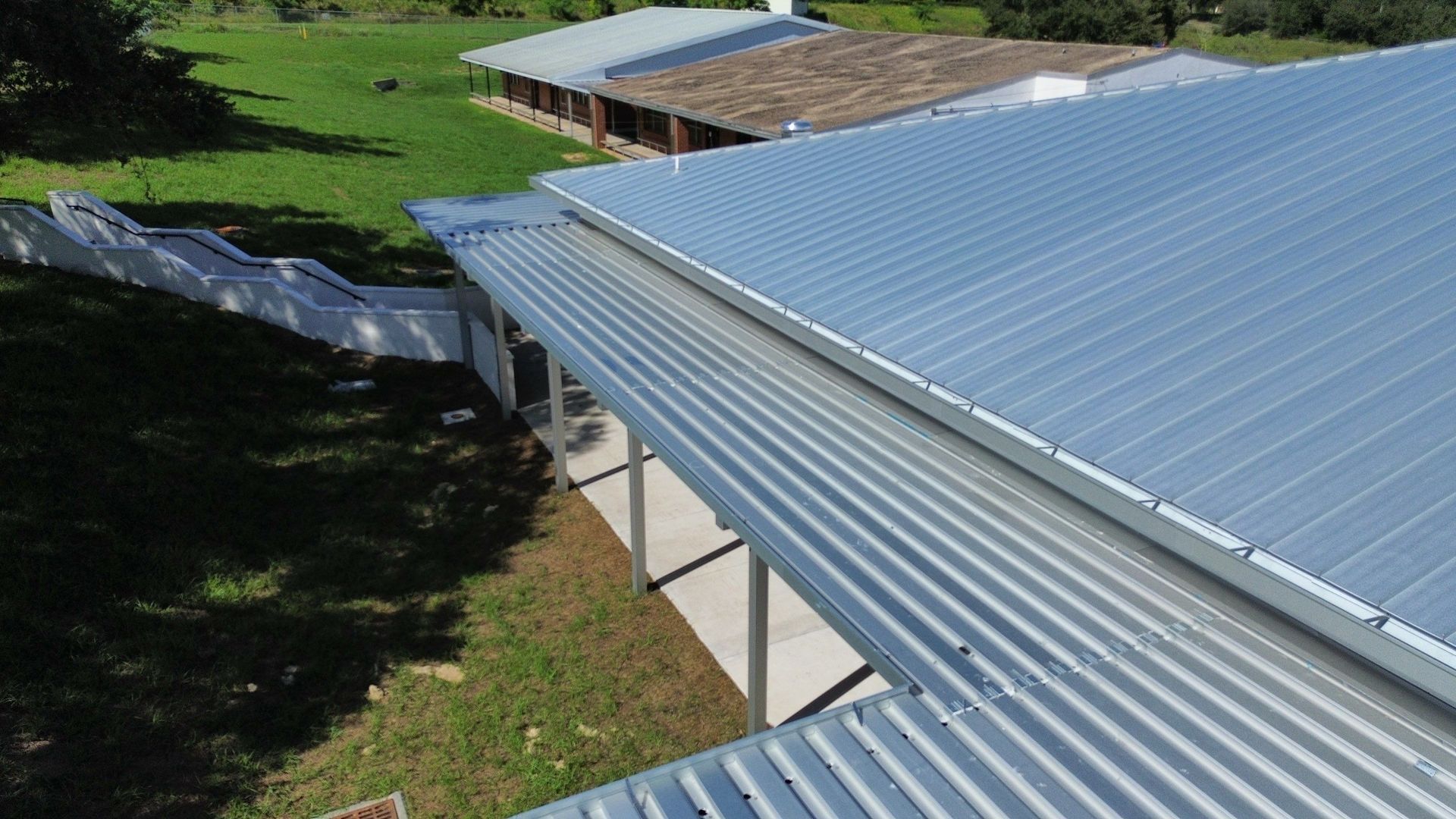 Corrugated metal rooftops beside a grassy yard and trees in bright sunlight