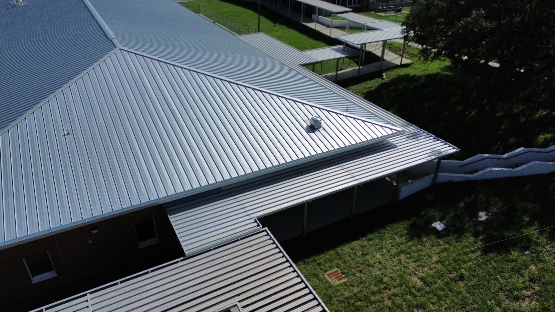 Silver metal roof with skylight beside a grassy yard and walkway, viewed from above