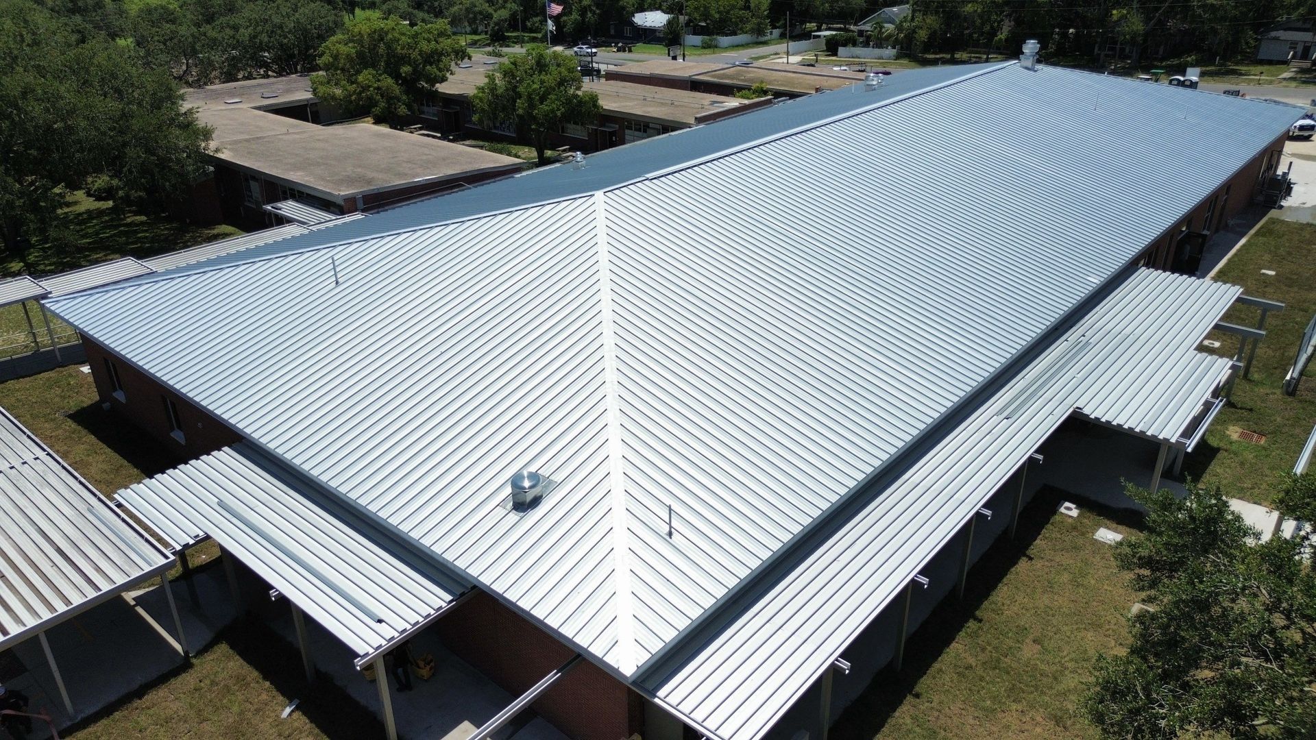 Aerial view of a large white corrugated metal roof on a house surrounded by trees.