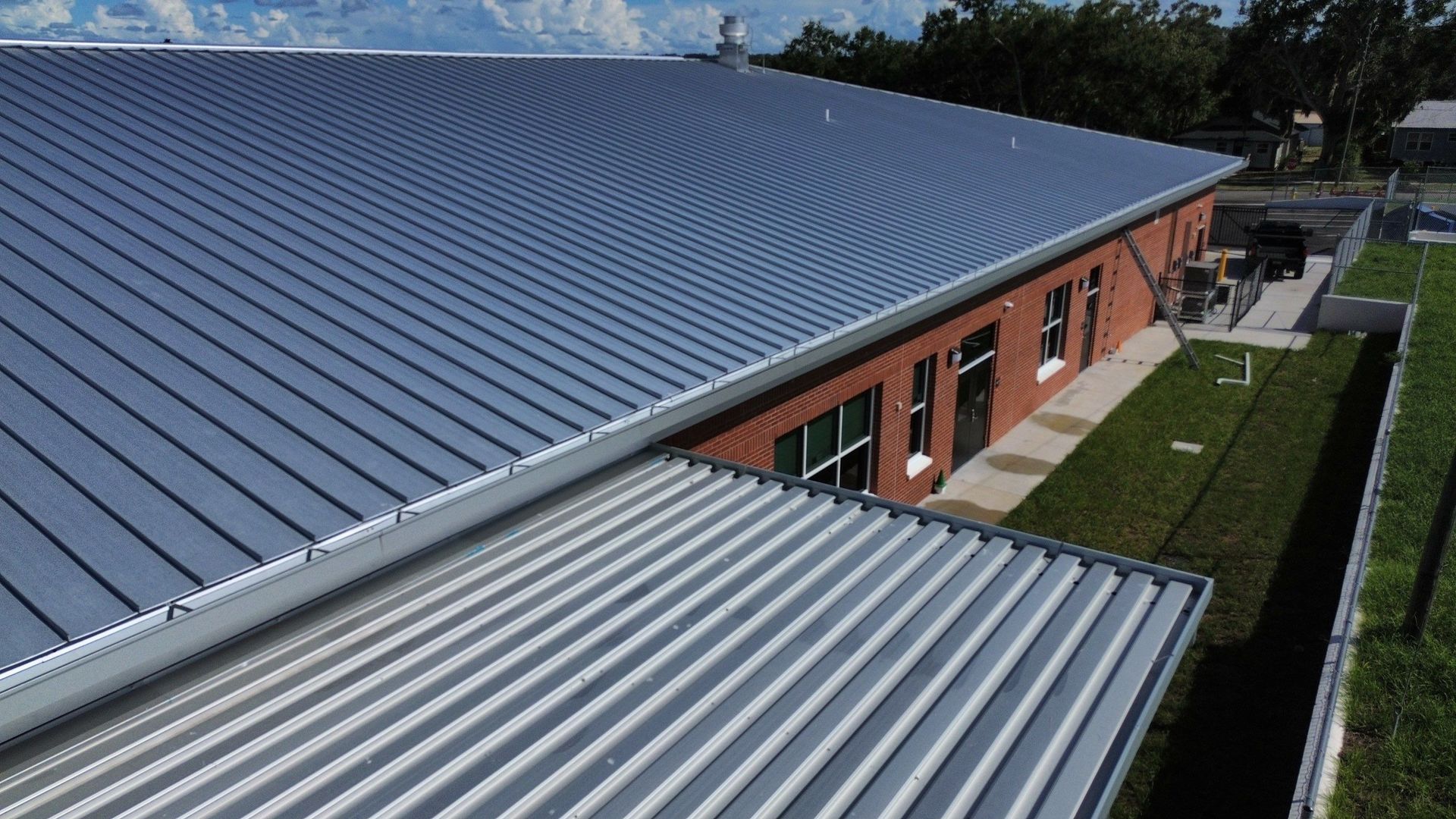 Long gray metal roof over a red brick building with a grassy walkway beside it