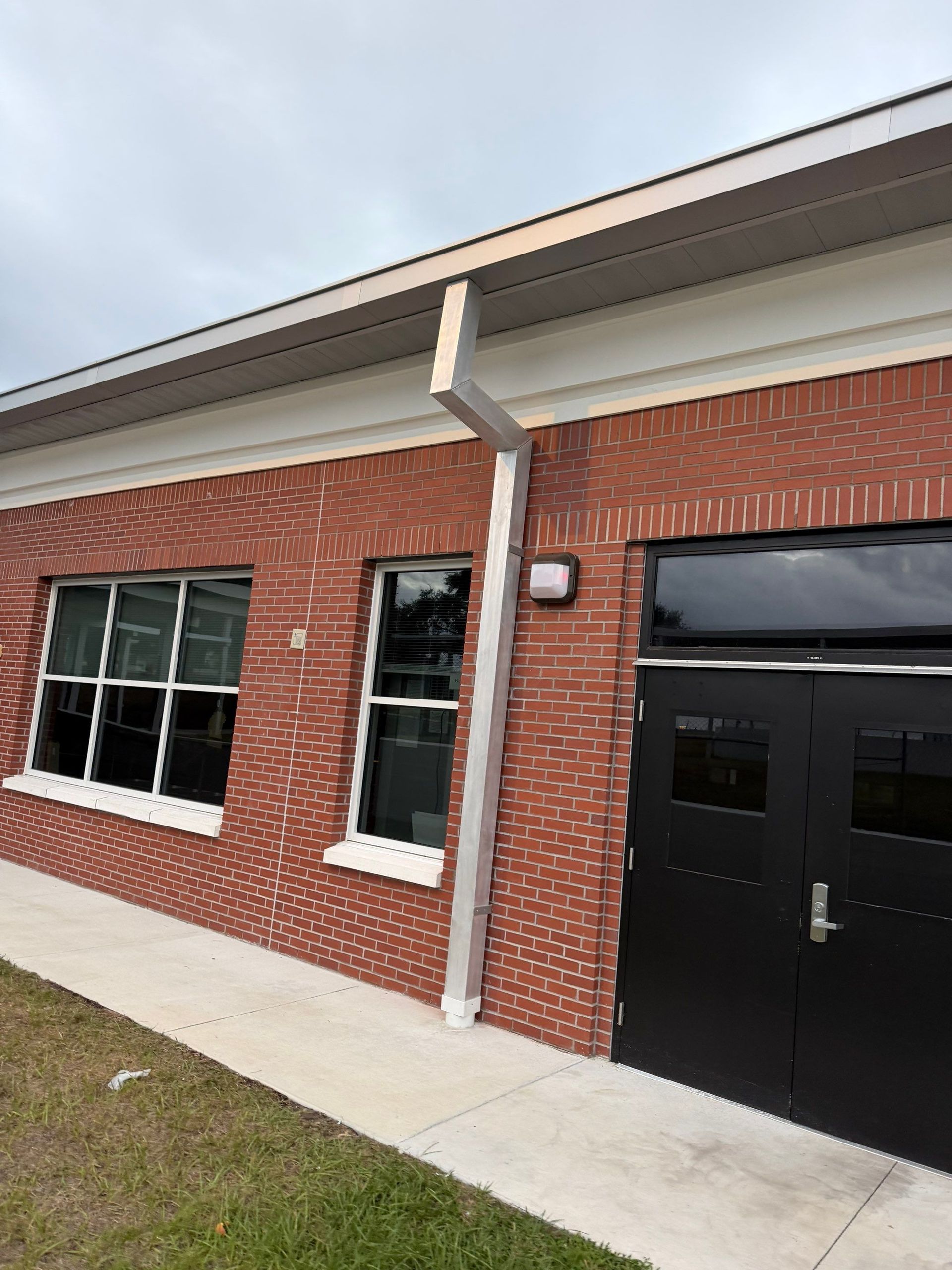 Brick building exterior with windows, a black door, and a covered entrance under a white roofline.