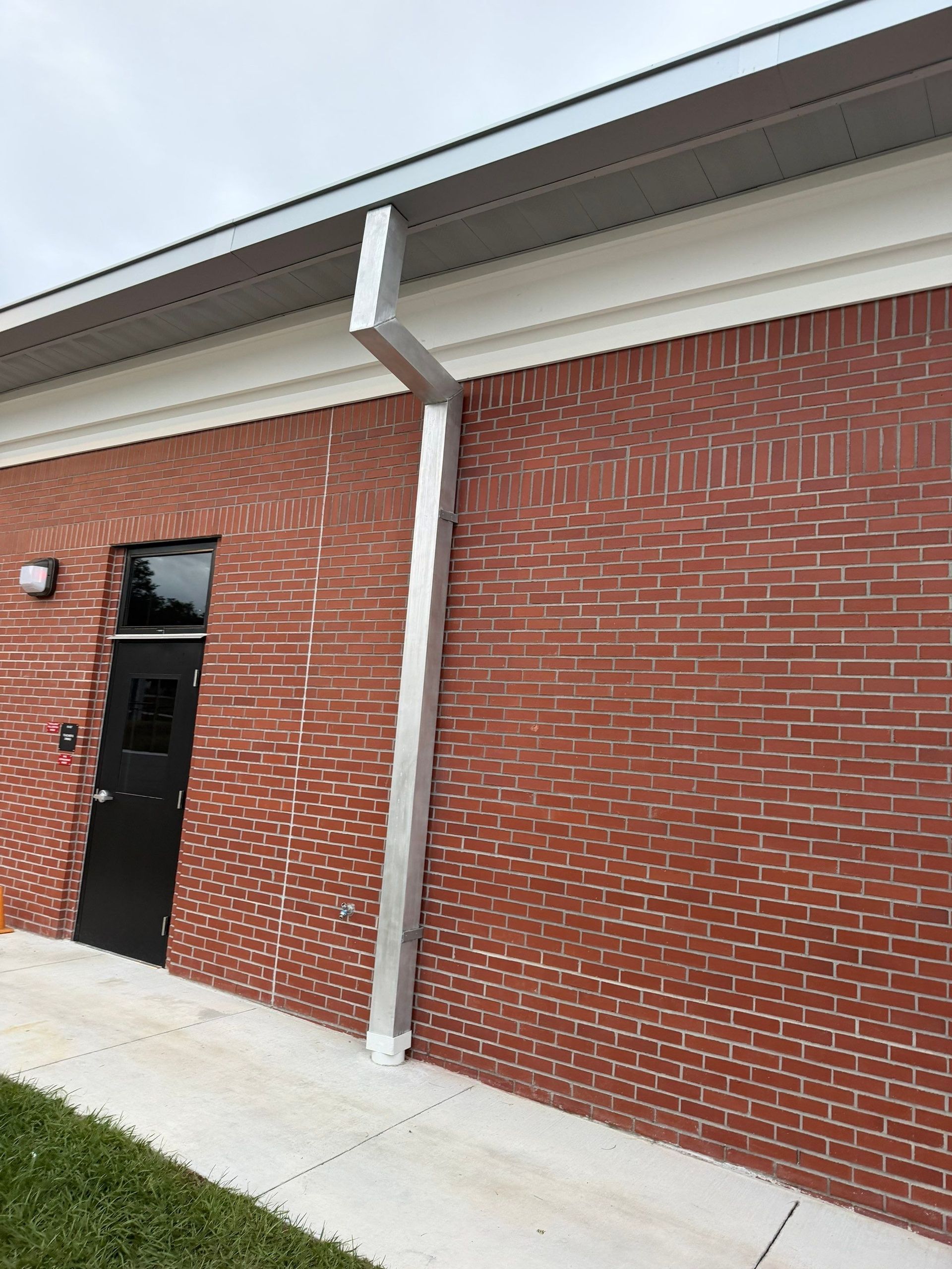 Brick building exterior with a black door, white downspout, and concrete walkway