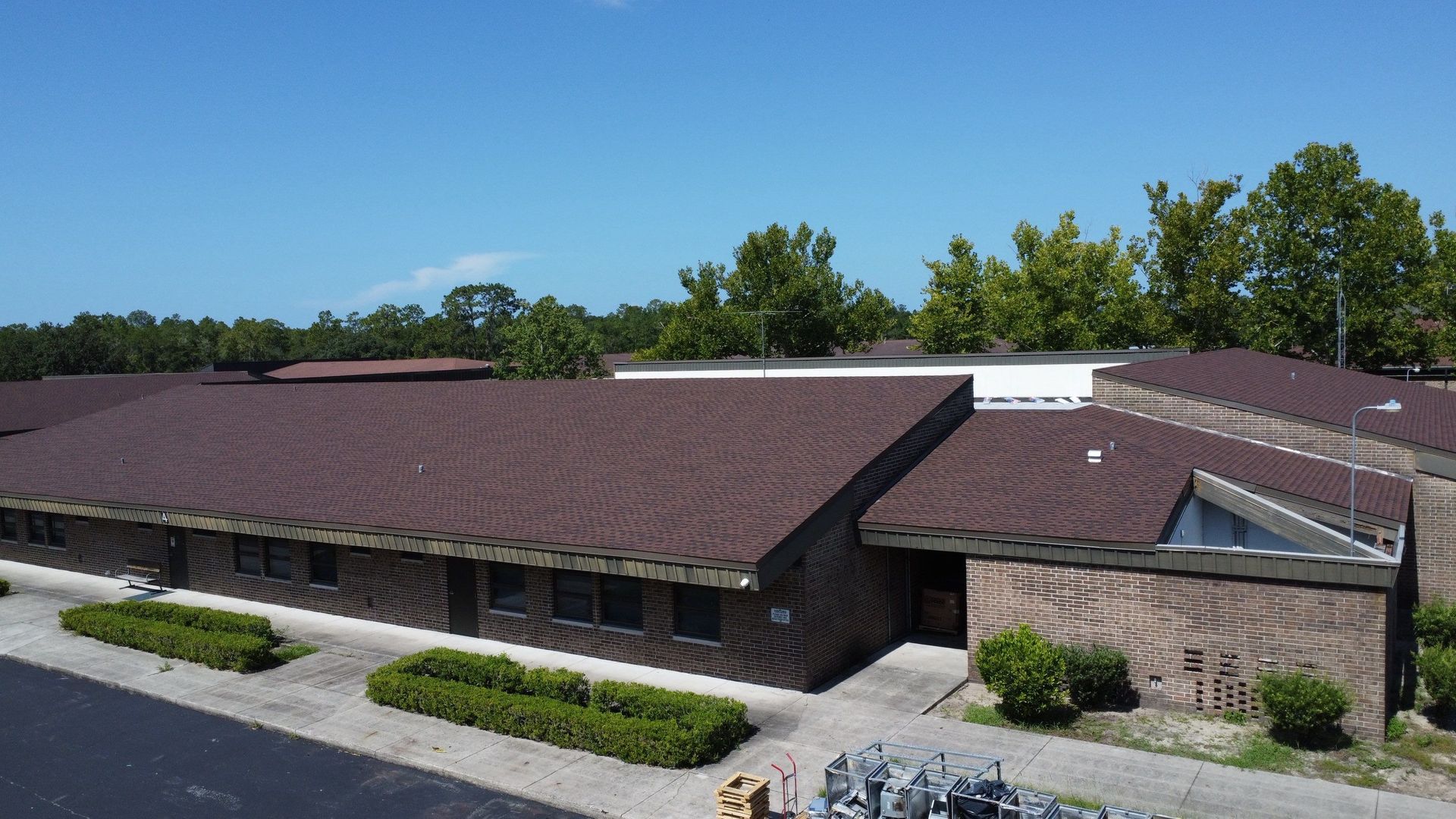 Low brick office building with a brown roof and shrubs along the front