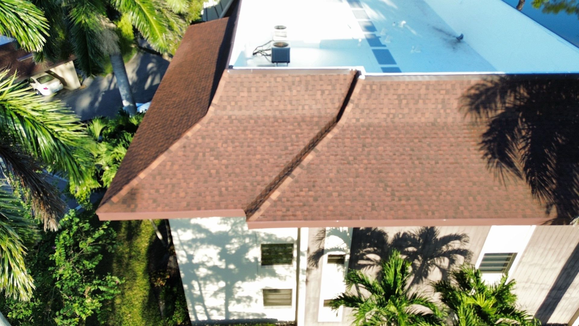 Aerial view of a tan-roofed house surrounded by palm trees beside a bright blue pool.