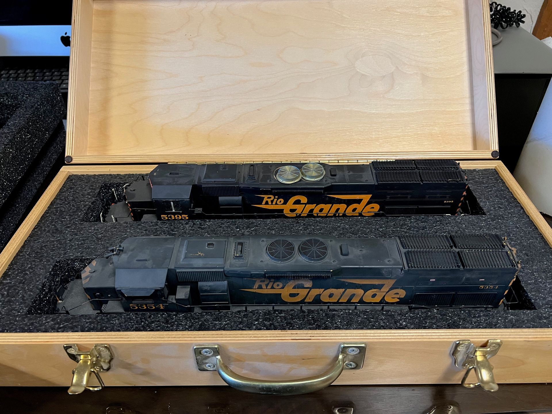 Wooden case holding two black model trains with gold lettering, arranged in foam padding.
