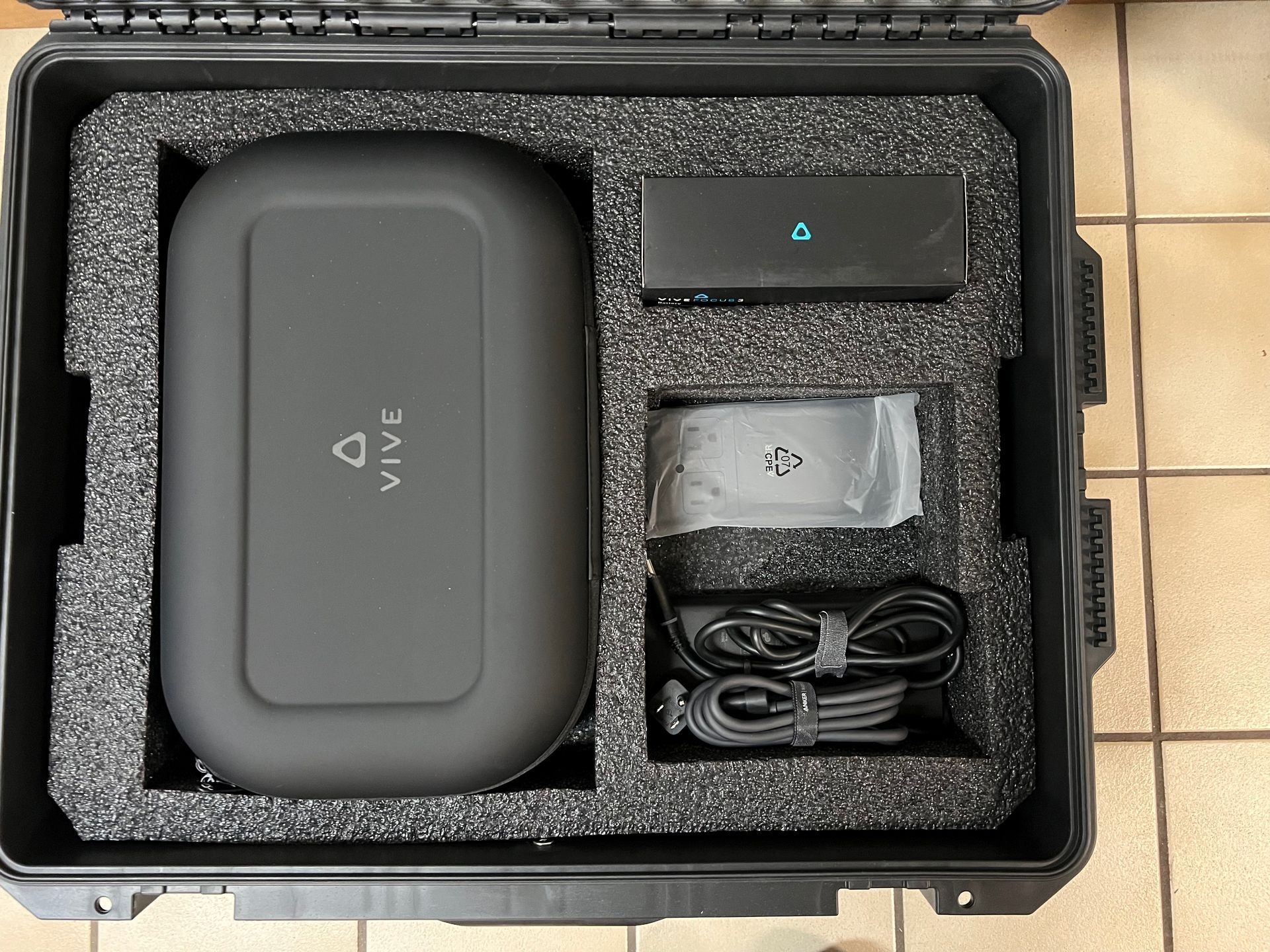 Open black case with foam insert holding a gray device, charger, and coiled cable.
